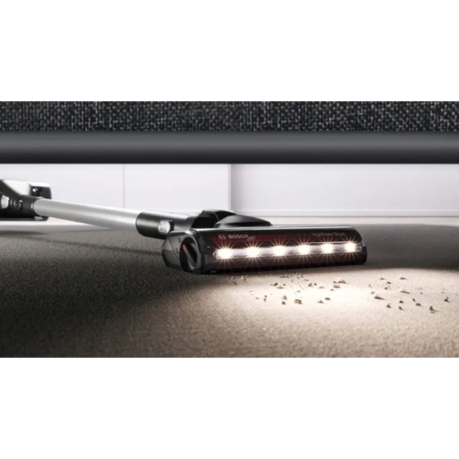 Gros plan sur une tête d'aspirateur sur un tapis. La tête est équipée de lumières qui éclairent le tapis et de petits débris.