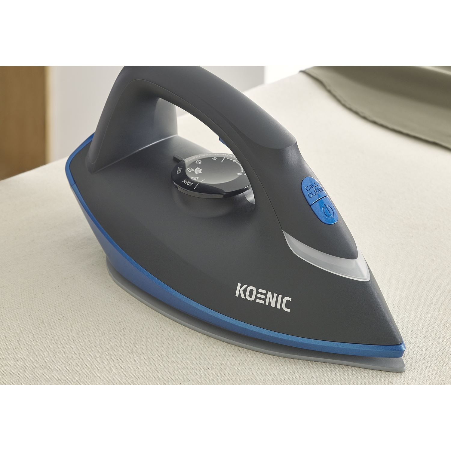 Un ferro da stiro Koenic nero e blu, su un asse da stiro beige. Presenta un quadrante e un pulsante blu 'Calc Clean'.