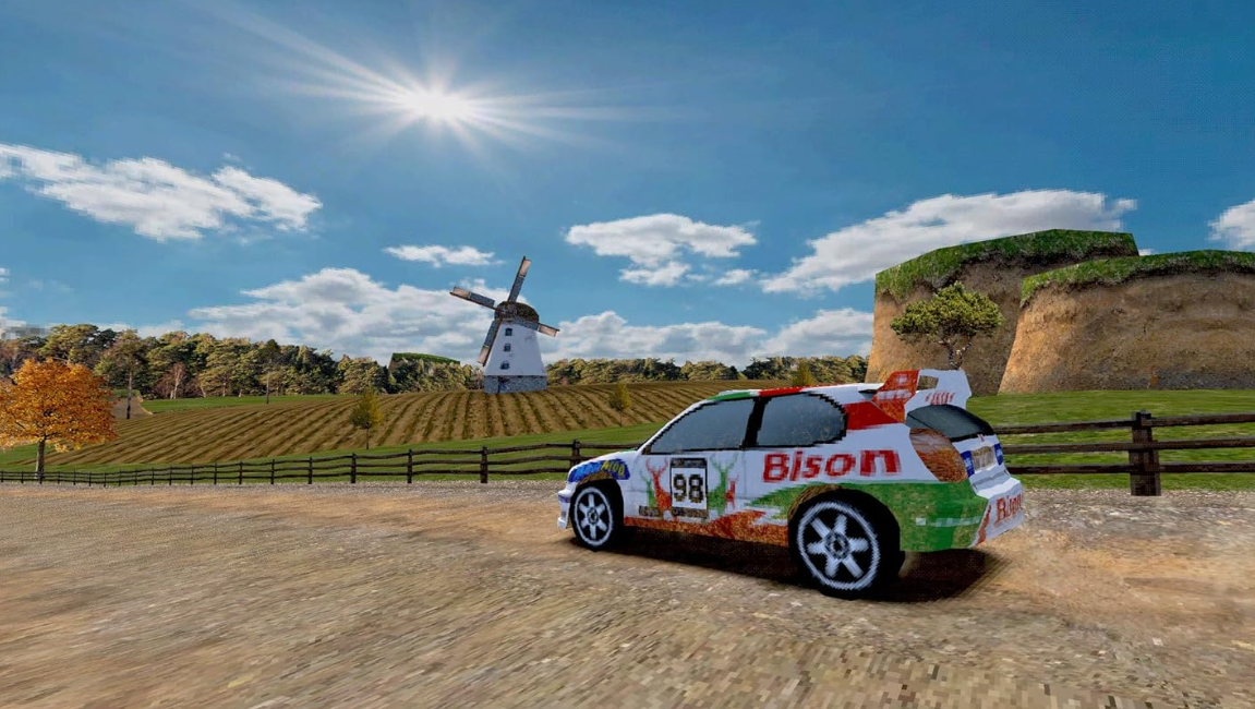 Ein Rallye-Auto auf einer unbefestigten Straße, mit einer Windmühle und Ackerland im Hintergrund unter blauem Himmel.