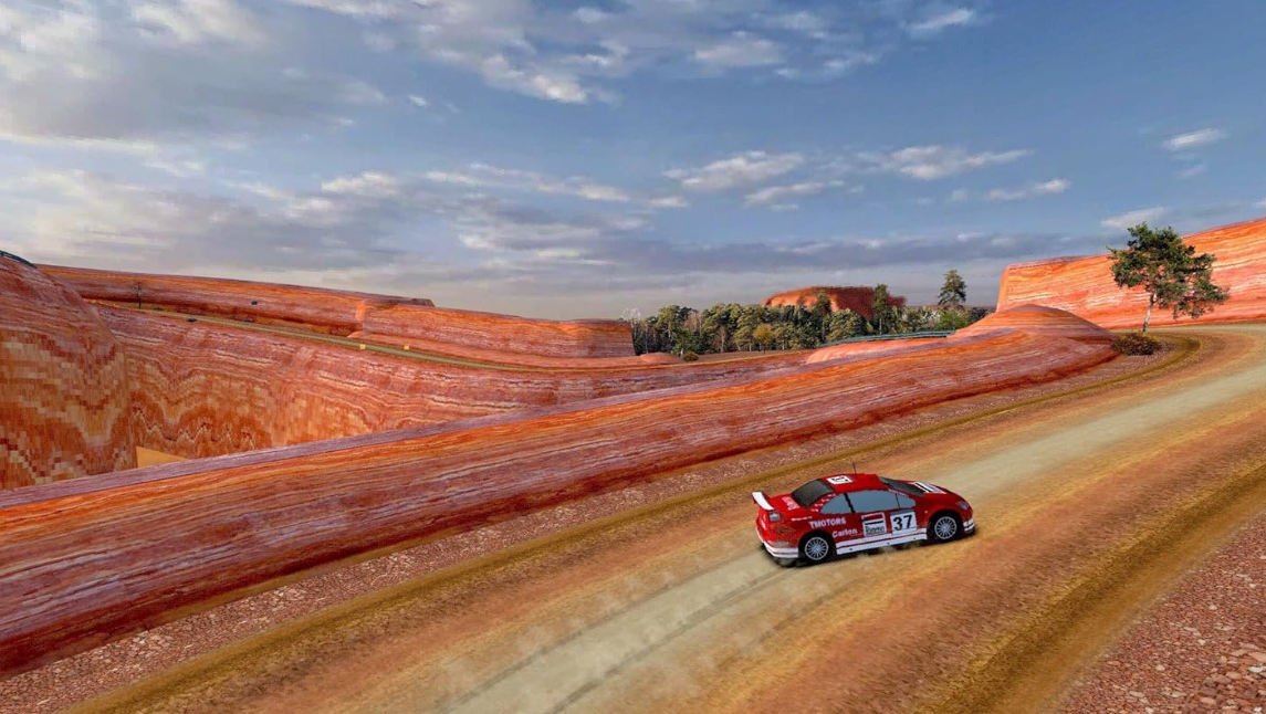 Ein rotes Rennauto fährt auf einer Schotterstraße durch einen Canyon. Die Landschaft zeigt rote Felsformationen und einen blauen Himmel.