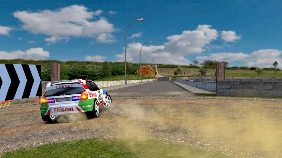 Ein Rallyeauto driftet auf einer Schotterstraße. Das Auto ist weiß mit grünen und roten Akzenten. Bäume und blauer Himmel im Hintergrund.