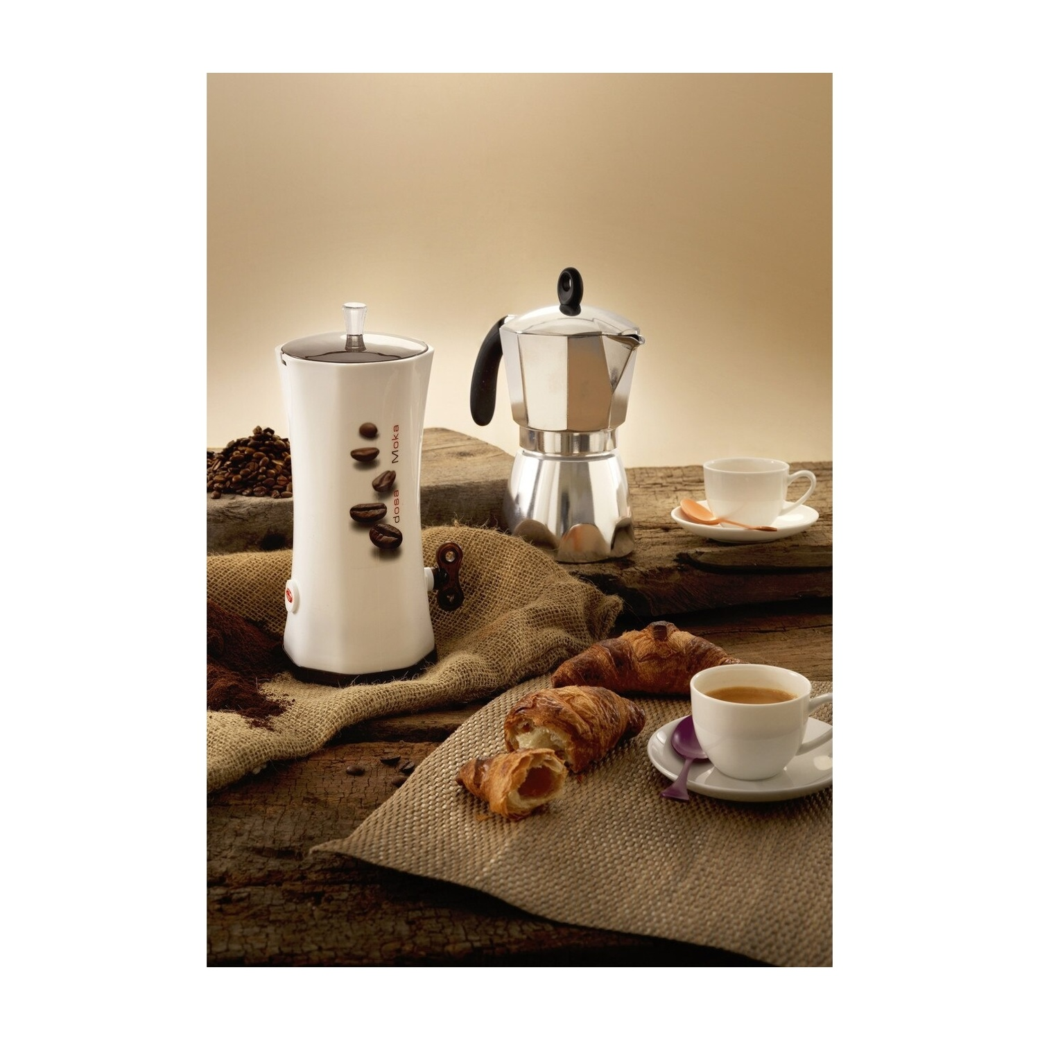Allestimento caffè: moka, macchina da caffè bianca, tazze, croissant e chicchi di caffè su un tavolo di legno.