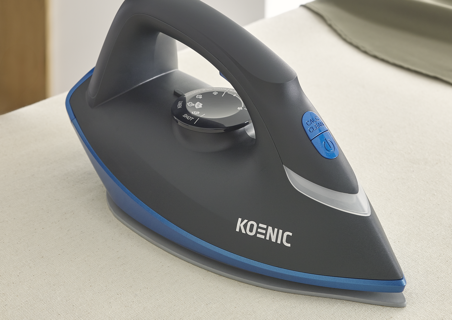Una plancha negra y azul sobre una superficie beige. La plancha tiene un asa, un dial y un botón azul. La marca es visible.