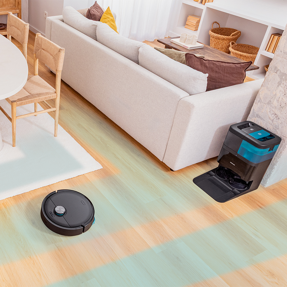 Un salón con un robot aspirador en un suelo de madera. Se ven un sofá, sillas y una estación de limpieza.