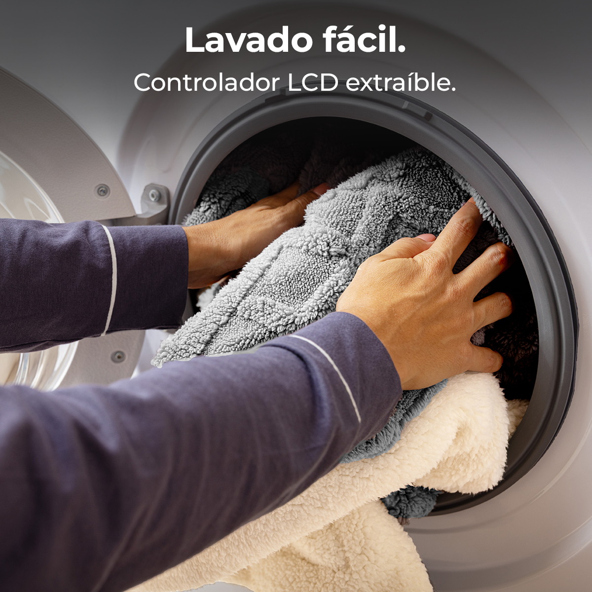 Manos colocando mantas grises y blancas en una lavadora. El texto superior dice 'Fácil lavado'.