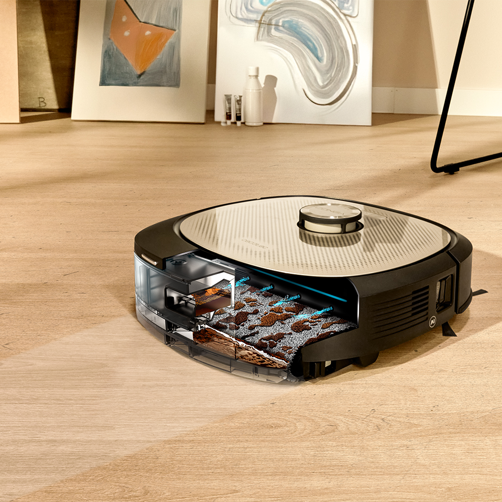 Una aspiradora robot negra y plateada con una vista seccionada. Sobre un suelo de madera, con cuadros al fondo.