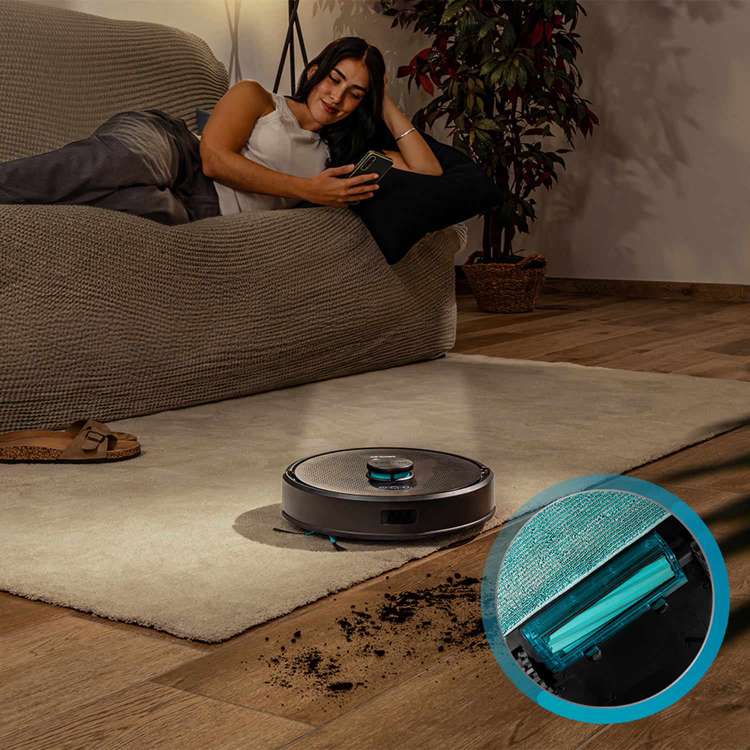 Mujer en sofá usa teléfono. Robot aspirador limpia alfombra. Suciedad en el suelo. Planta en el fondo.