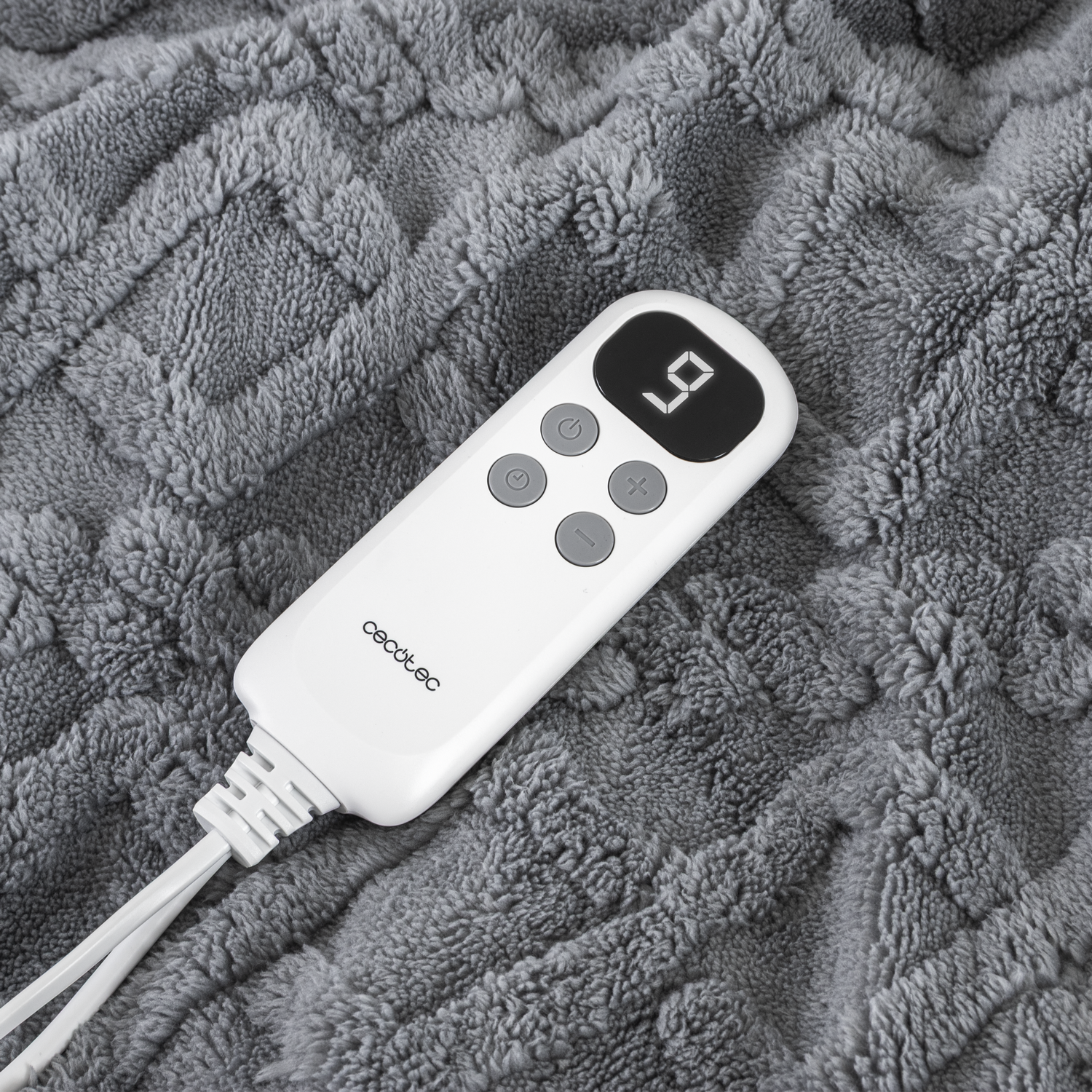 Un controlador blanco de manta térmica con pantalla digital que muestra '9' sobre una manta gris texturizada.