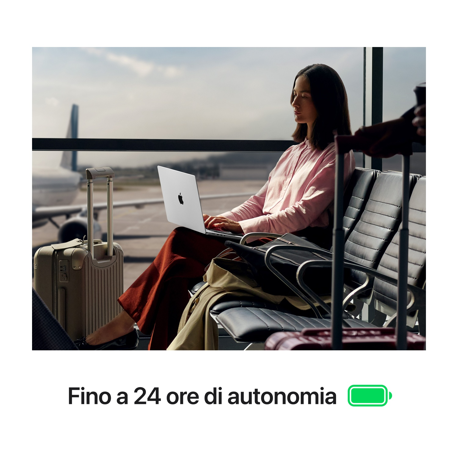 Una donna usa un laptop in aeroporto. Sono visibili bagagli e un aereo. L'immagine ha un testo sulla durata della batteria.