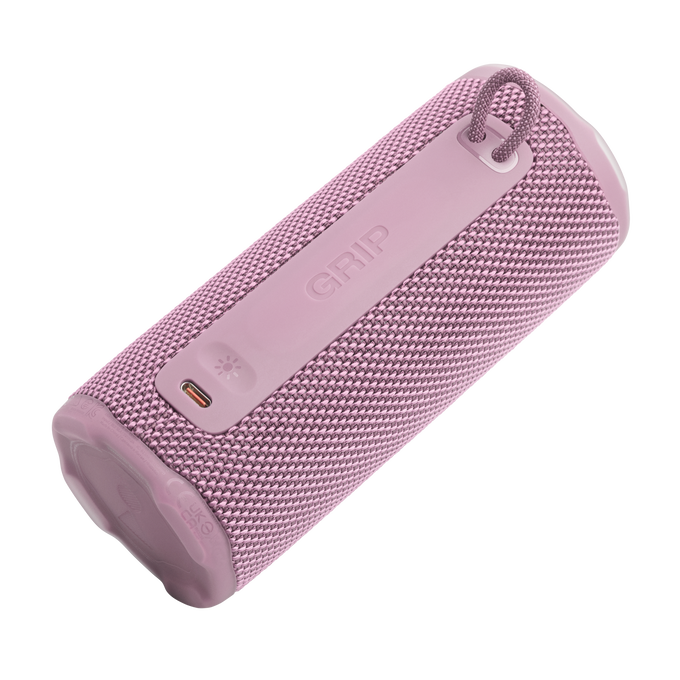 Un altavoz cilíndrico rosa con textura de tela. Tiene un asa, un panel de control con la palabra 'GRIP' y un puerto de carga.
