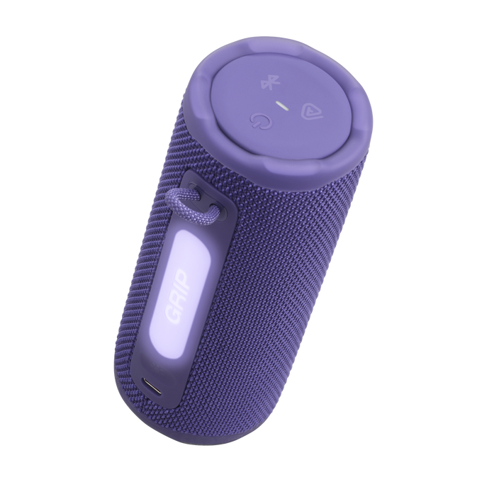 Un altavoz cilíndrico púrpura con botones superiores y una etiqueta 'GRIP'. Tiene una textura de tela y un lazo para una correa.