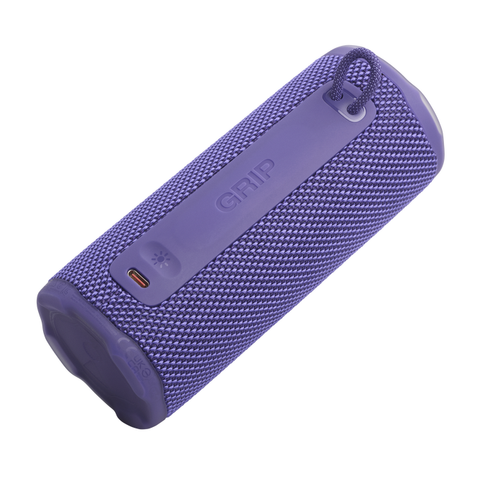 Un altavoz cilíndrico púrpura con textura de tela. Tiene una correa y la palabra "GRIP". Son visibles una luz y un puerto de carga.