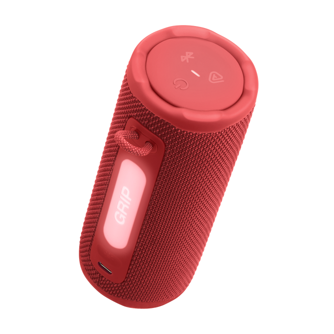 Un altavoz cilíndrico rojo con controles en la parte superior y una etiqueta 'GRIP'. Tiene una textura de tela y un asa. El fondo es negro y dorado.