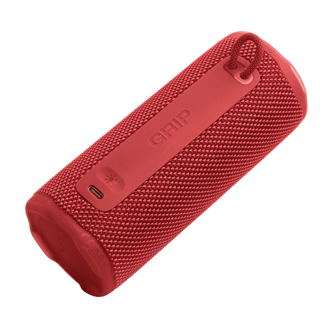 Altavoz cilíndrico rojo con asa. La palabra 'GRIP' es visible. Tiene un botón de encendido y un puerto de carga.