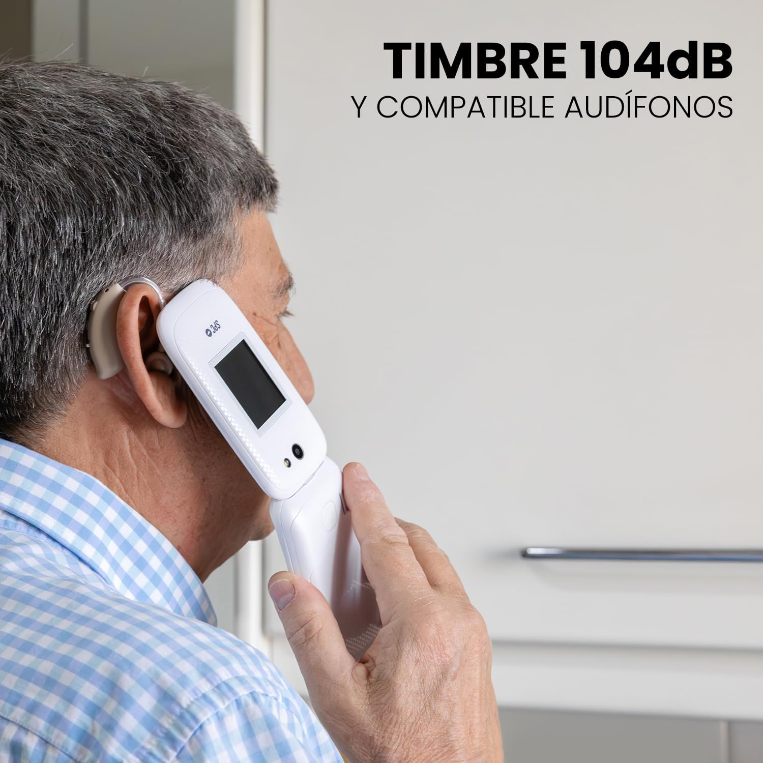 Un hombre con audífono sostiene un teléfono plegable blanco en su oído. El teléfono tiene una pantalla y está abierto. El hombre viste una camisa azul.
