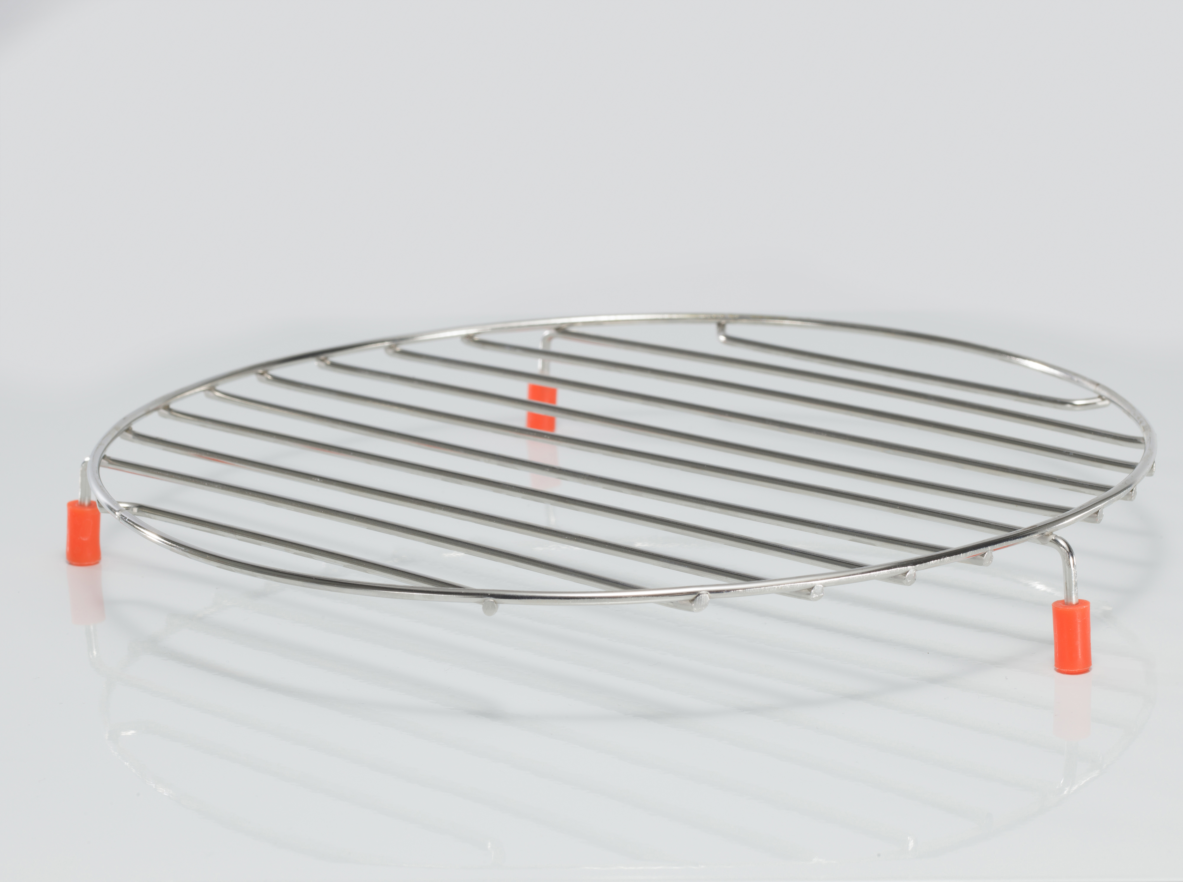 Okrągły, metalowy ruszt do chłodzenia z pomarańczowymi wspornikami na białej powierzchni, odbijający światło.
