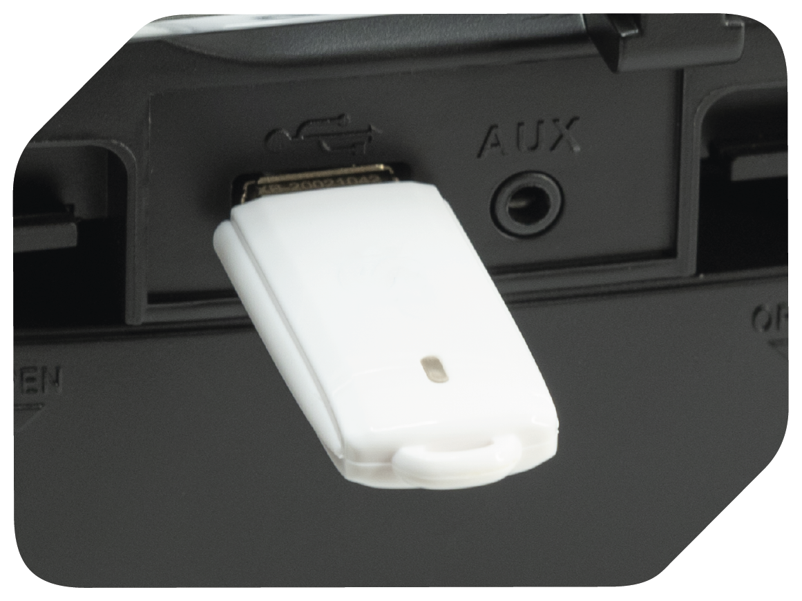 Biały adapter USB jest podłączony do czarnego urządzenia. Widoczne jest słowo AUX. Adapter ma małe światło.