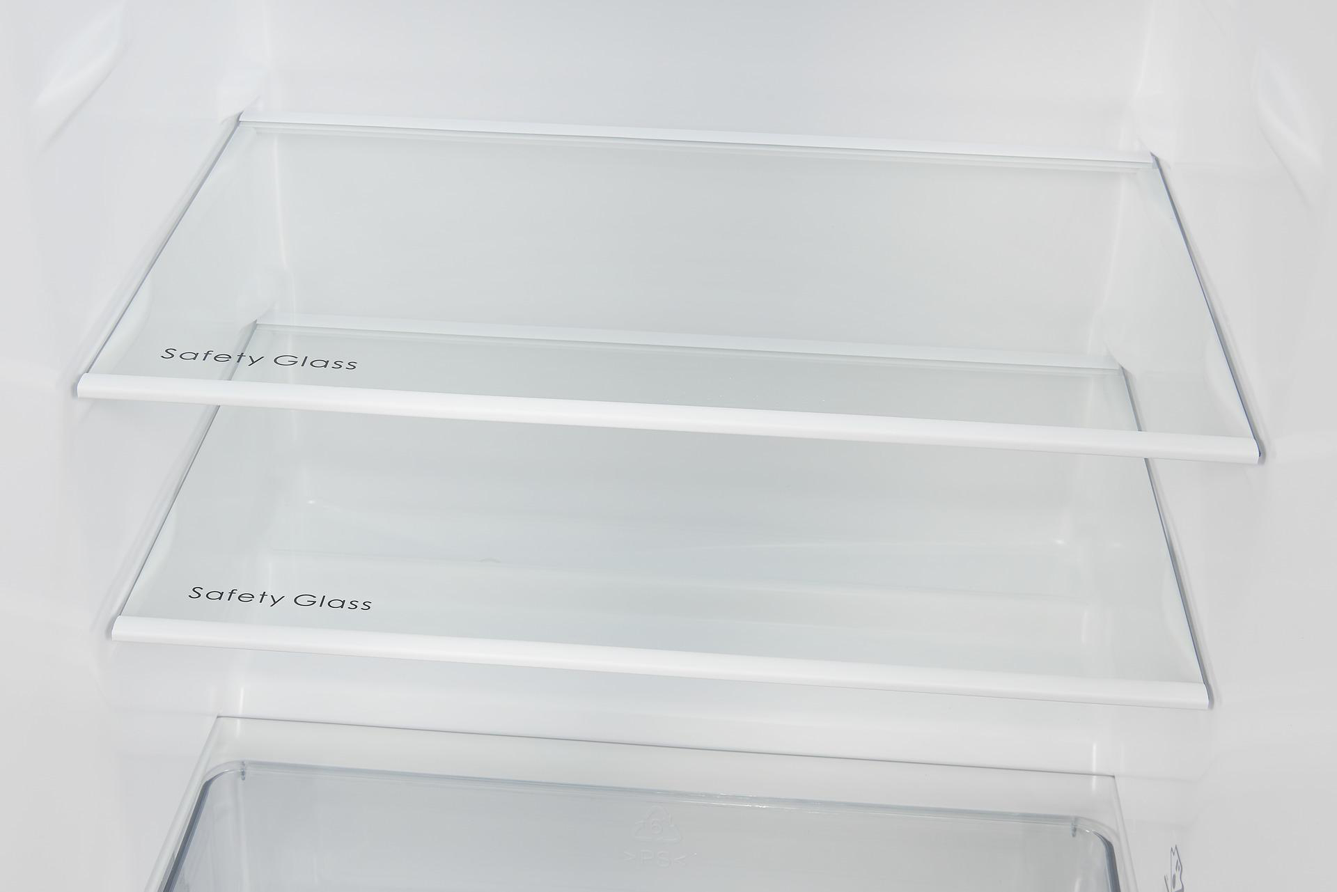 Im Inneren eines weißen Kühlschranks sind zwei Glasböden mit der Aufschrift 'Safety Glass' zu sehen. Der Boden hat eine Plastikschublade.