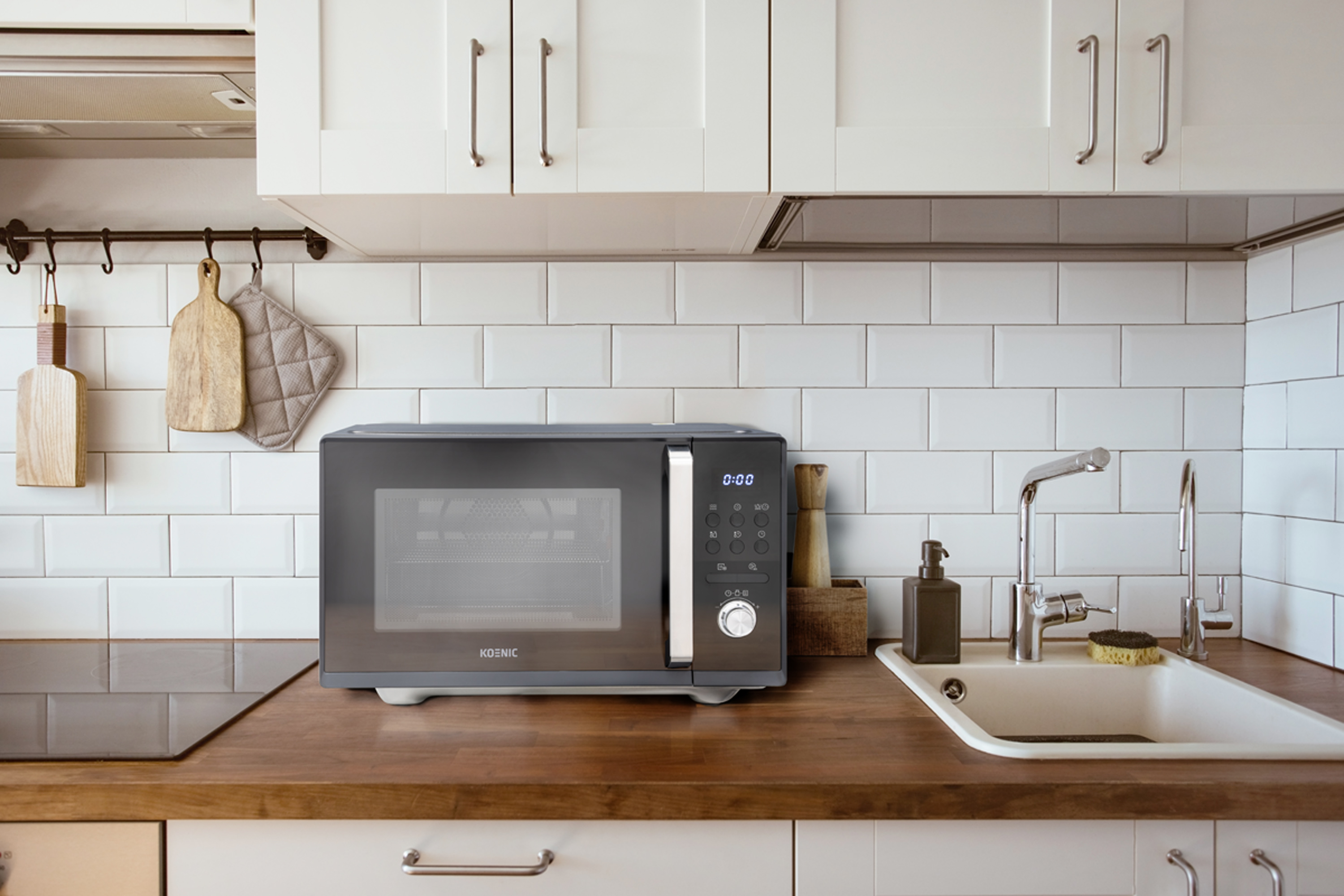 Nowoczesna kuchnia z kuchenką mikrofalową, zlewem i szafkami. Deski do krojenia i podkładka wiszą nad kuchenką.