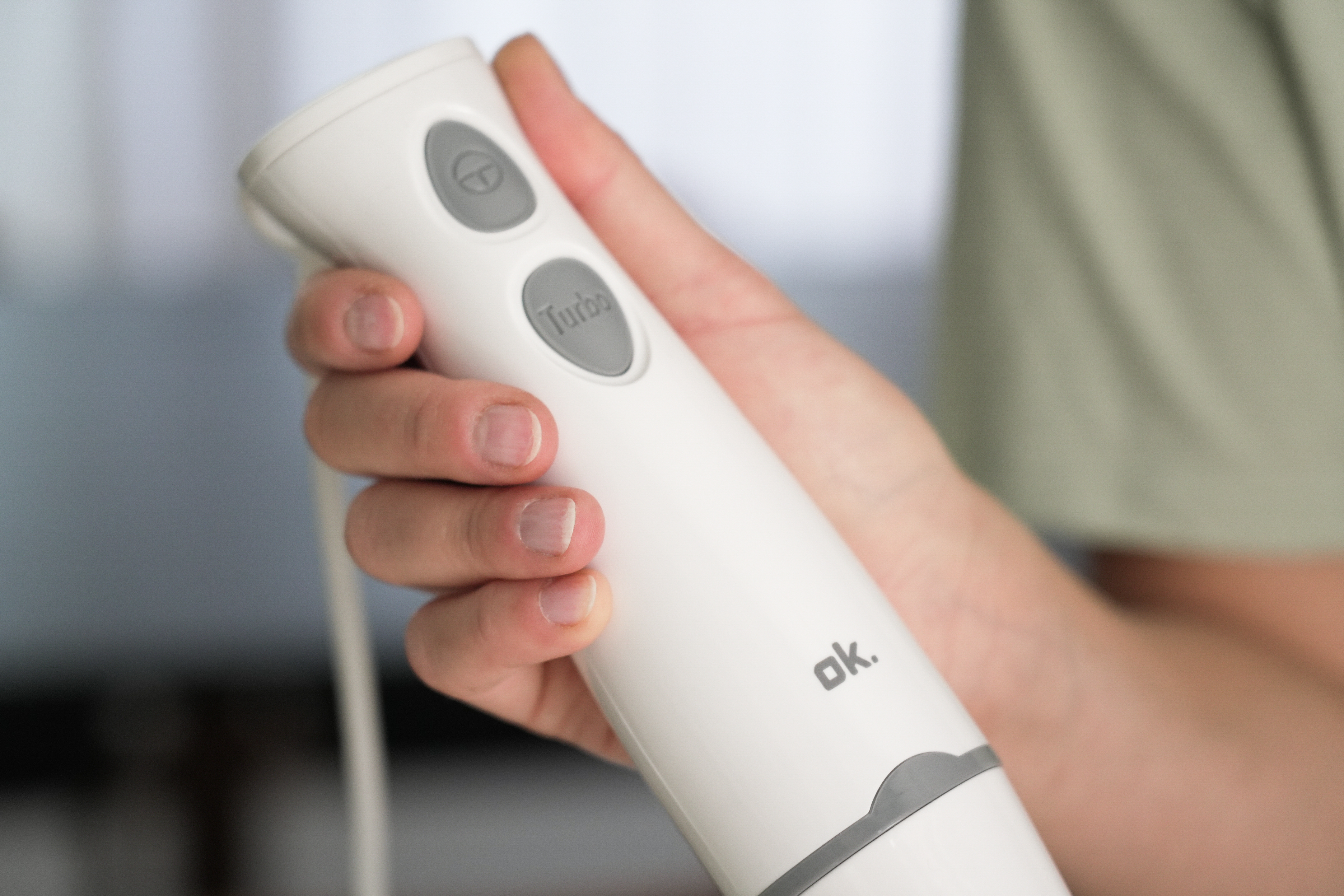 Ręka trzyma biały blender. Ma szare przyciski i widoczny jest napis 'ok'.