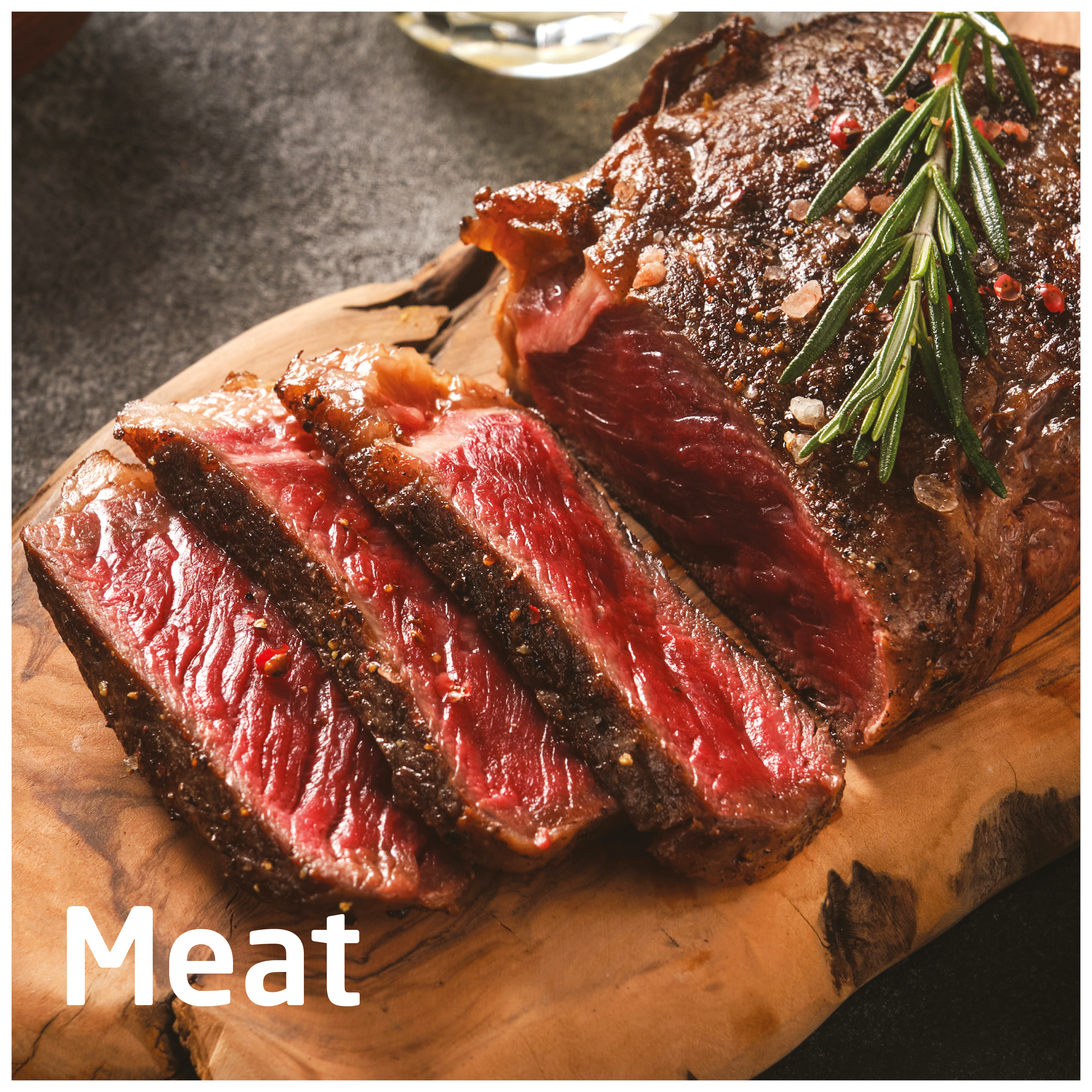 Krojony stek na drewnianej desce. Czerwone mięso z widocznym usłojeniem. Gałązka rozmarynu na wierzchu. Ciemne tło.