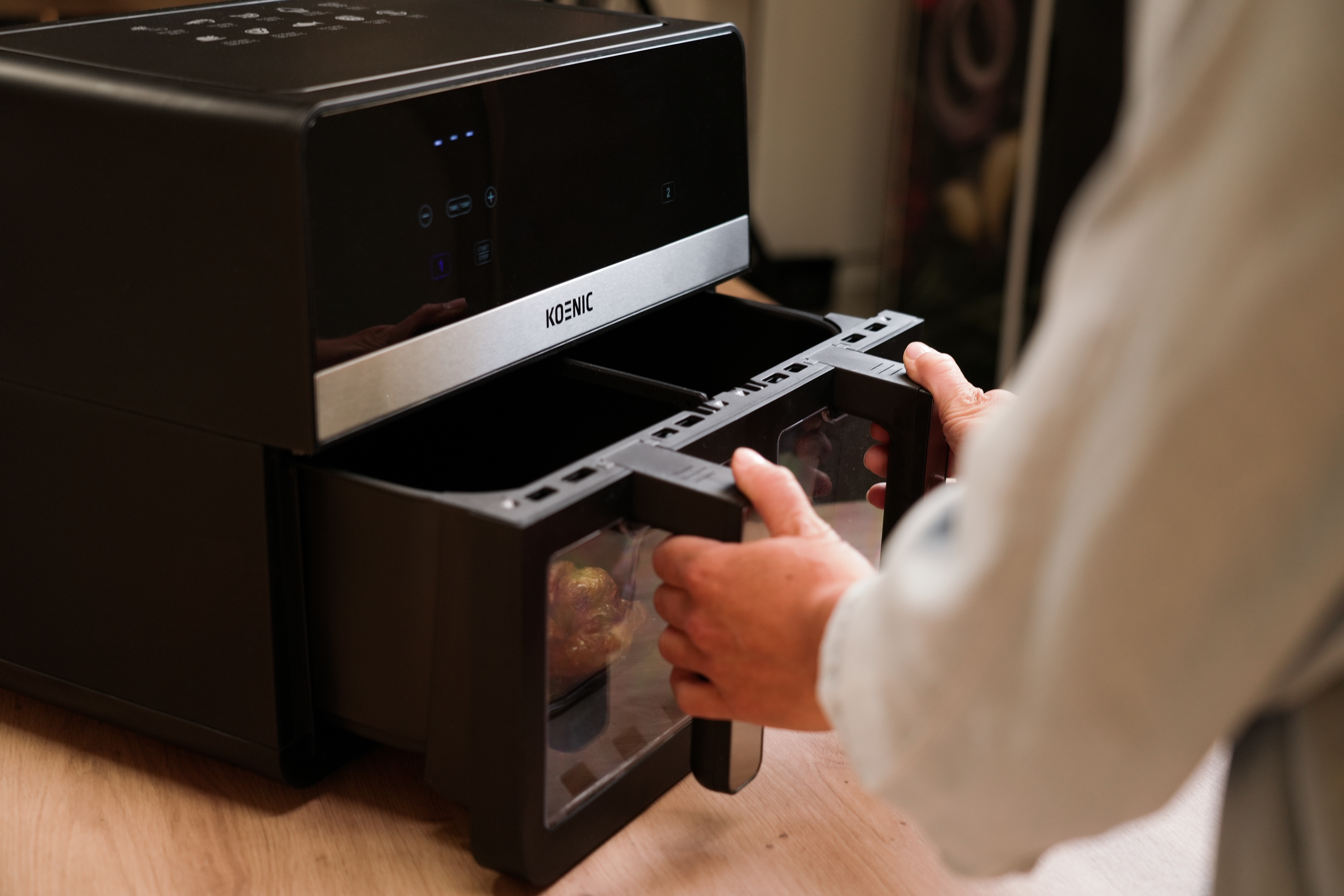 Osoba otwiera drzwiczki czarnej frytkownicy beztłuszczowej. Wewnątrz drzwi są warzywa.