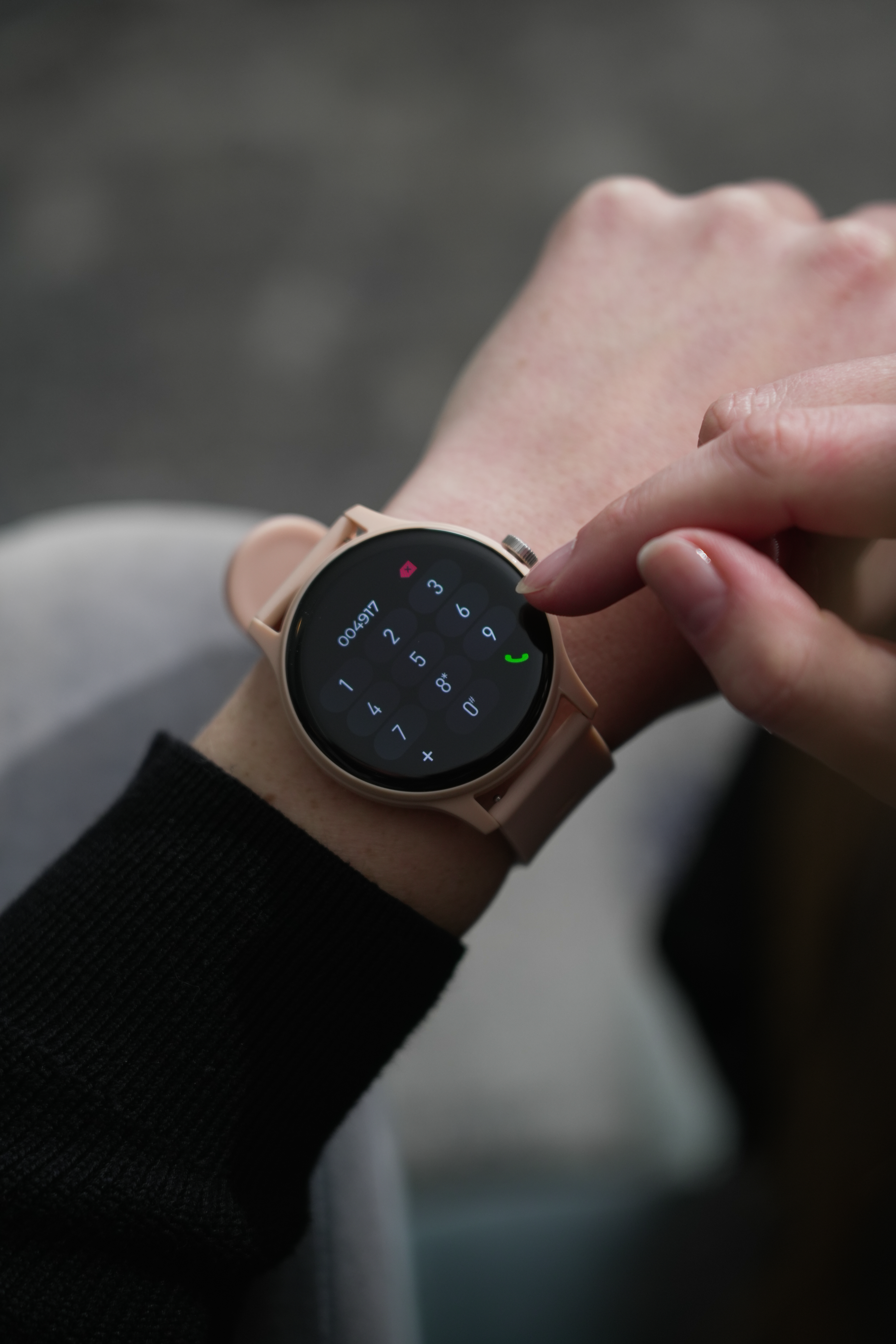 Handgelenk mit Smartwatch, die ein Ziffernfeld anzeigt. Ein Finger berührt die Anruftaste.