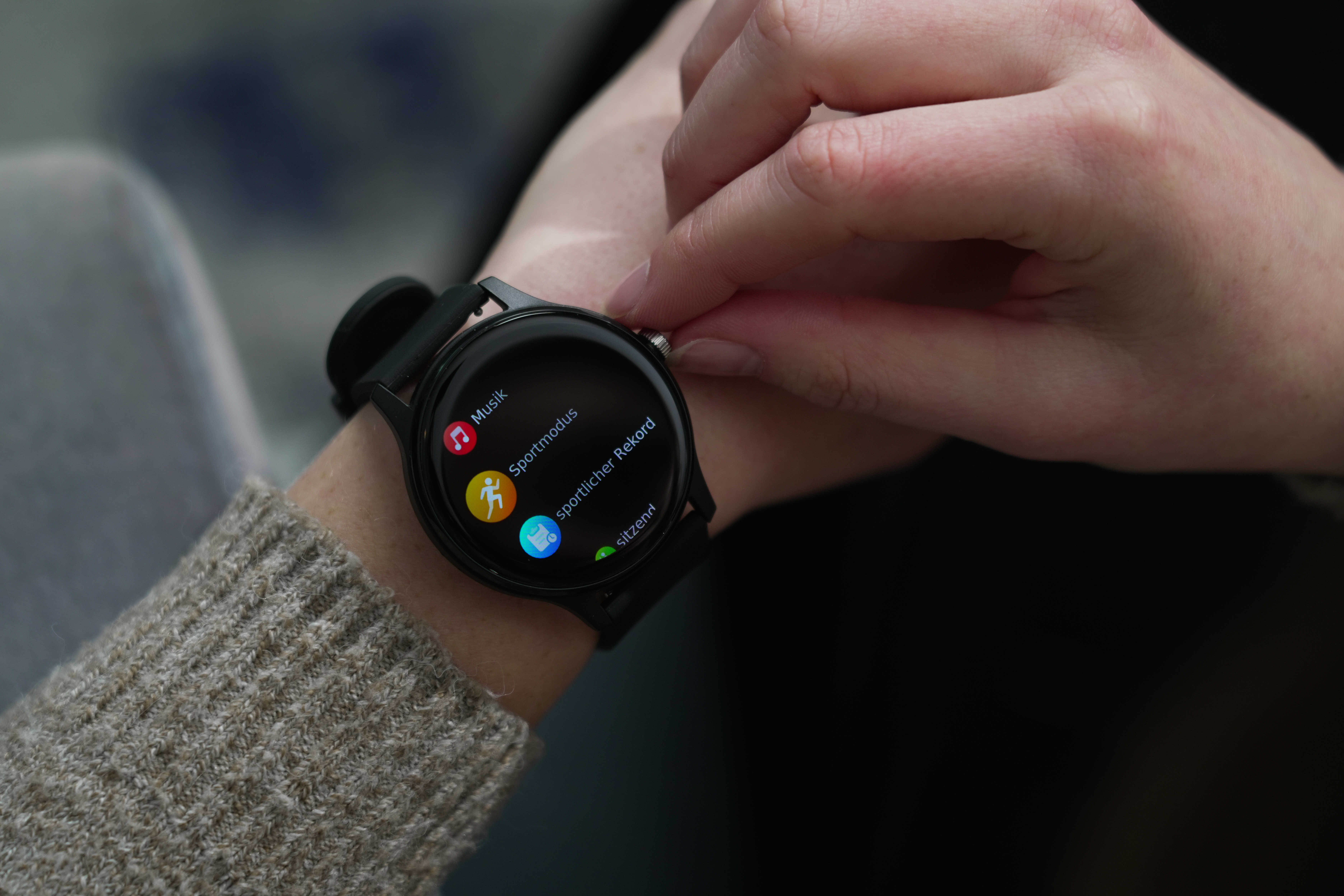 Ein Handgelenk mit einer Smartwatch. Die Uhr zeigt Optionen für Musik, Sportmodus und mehr an.
