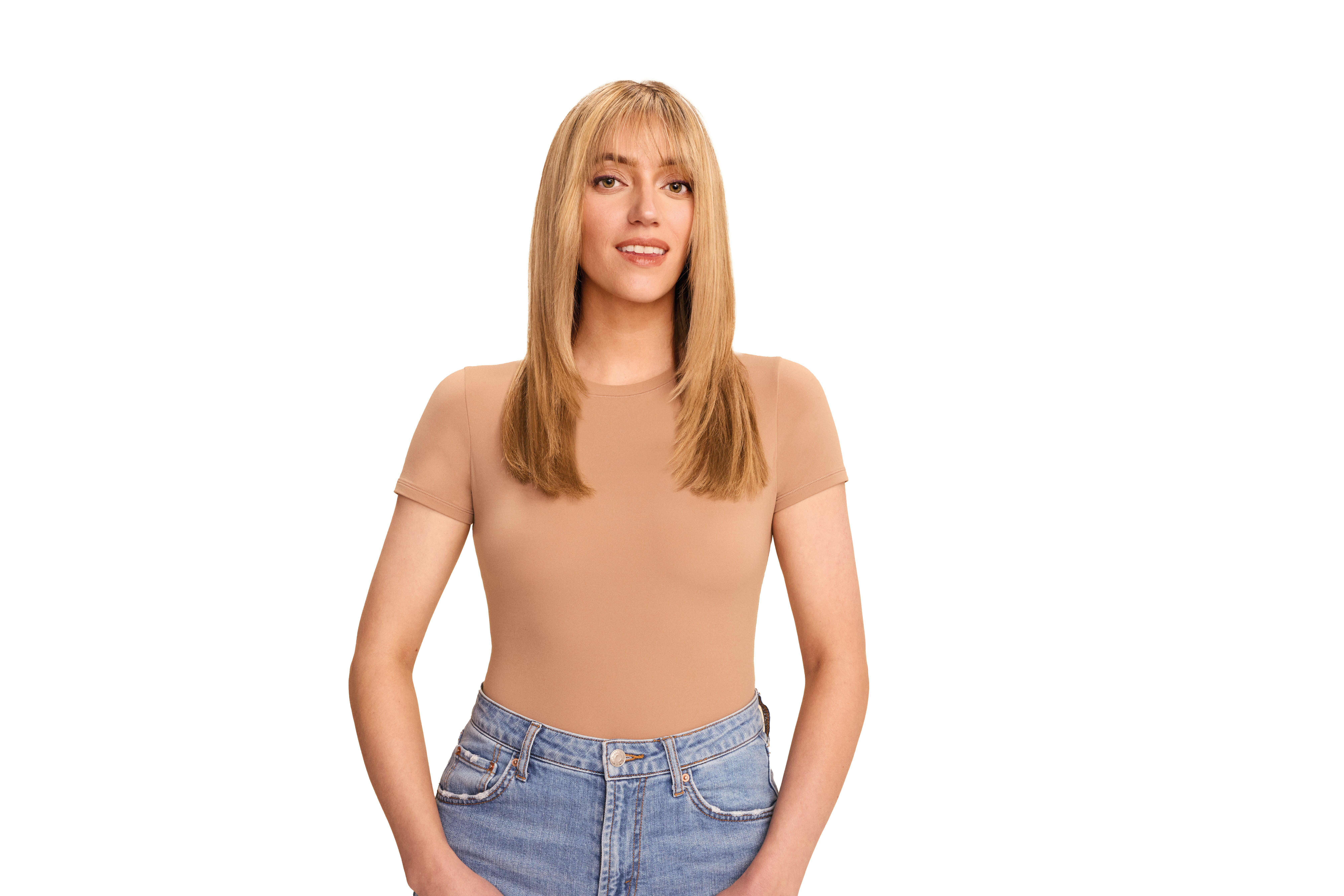 Eine Frau mit blondem Haar, beigem Oberteil und Jeans lächelt. Der Hintergrund ist weiß.