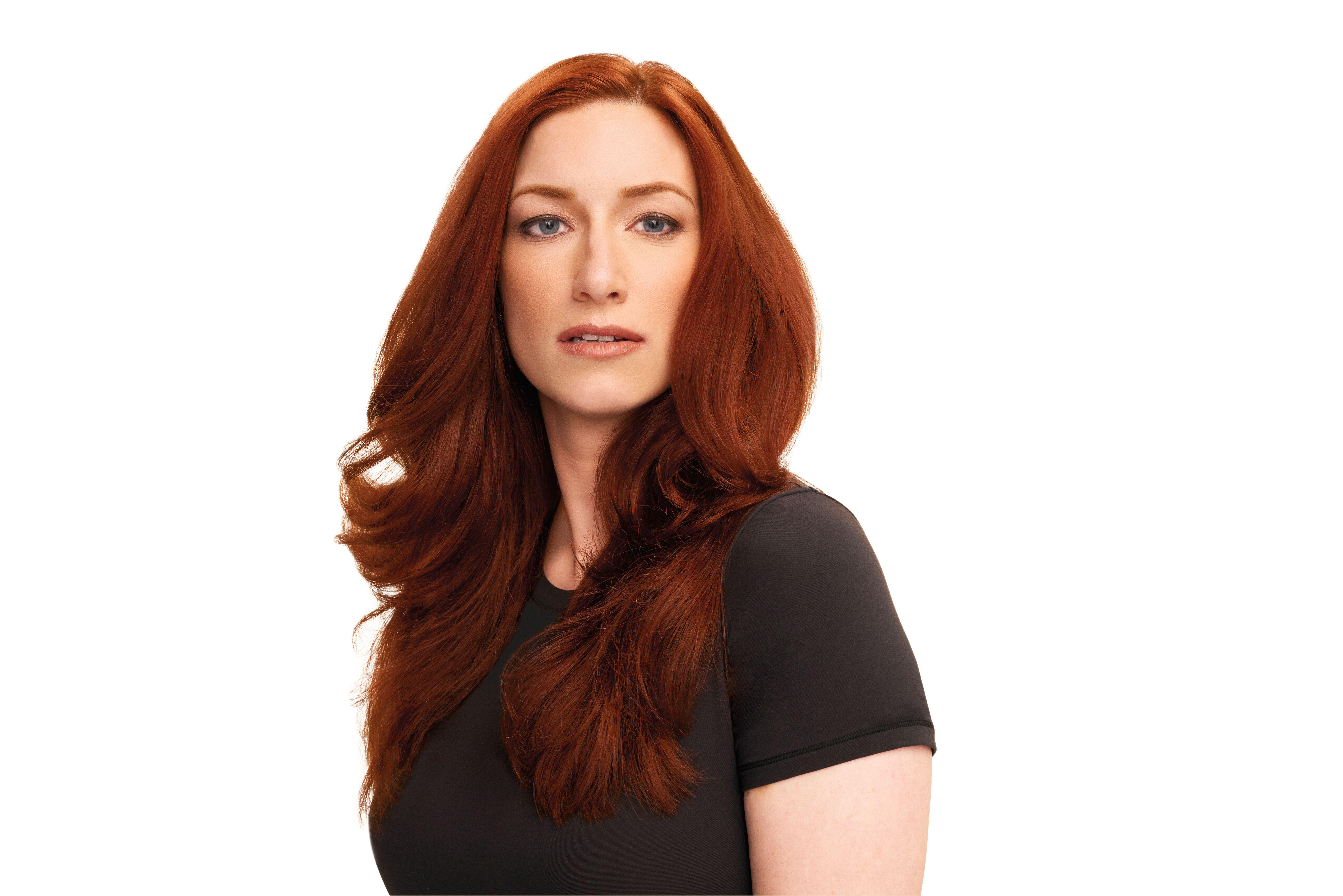 Eine Frau mit roten Haaren und blauen Augen, trägt ein schwarzes Oberteil vor weißem Hintergrund.