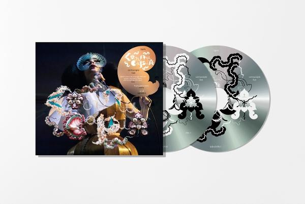 Albumcover und CDs. Sängerin mit Maske, hält eine Disc. Albumtitel und CD-Designs mit schwarz-weißen Mustern.