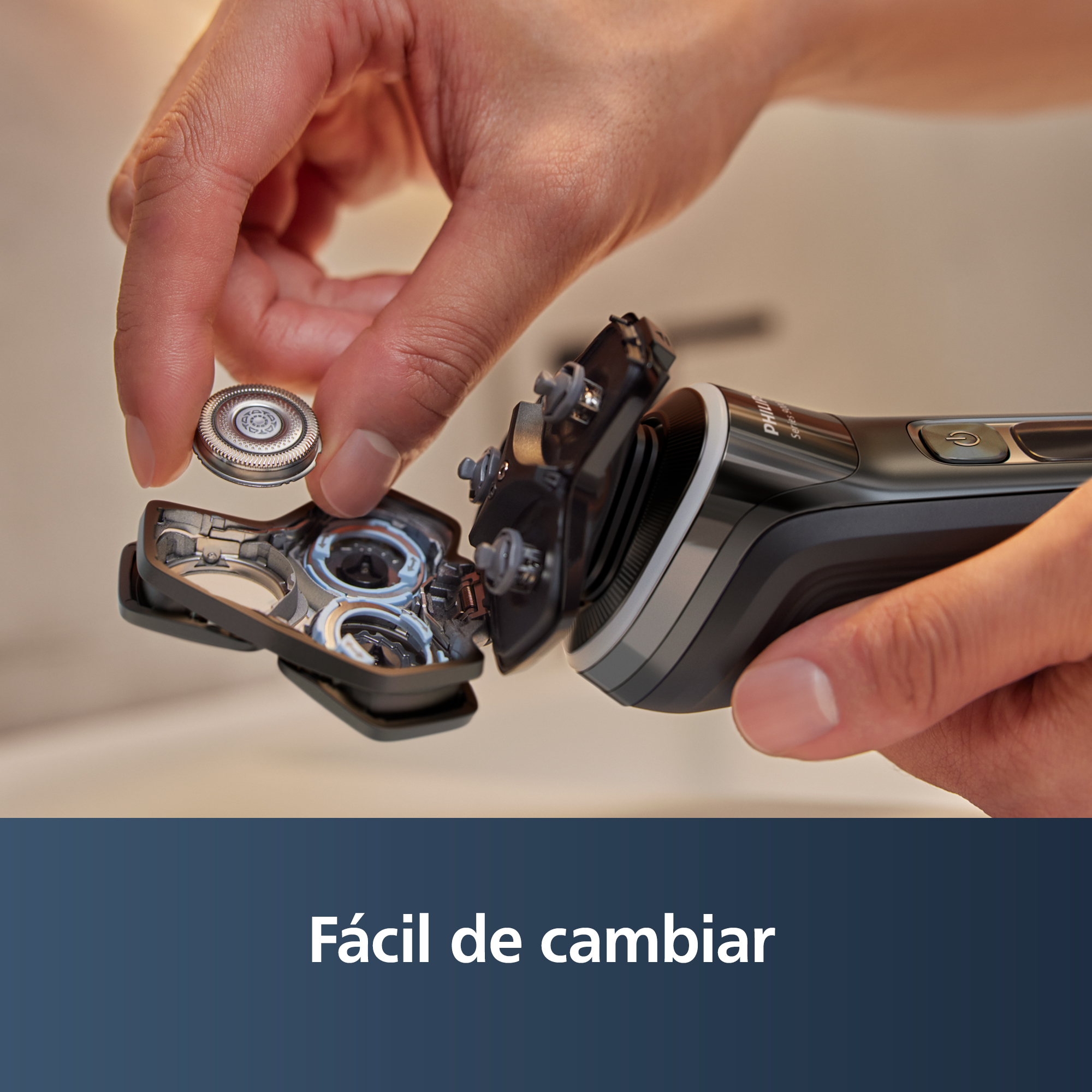 Una mano sostiene una pieza de afeitadora, mostrando cómo quitarla. La afeitadora es negra y plateada. Texto Fácil de cambiar abajo.