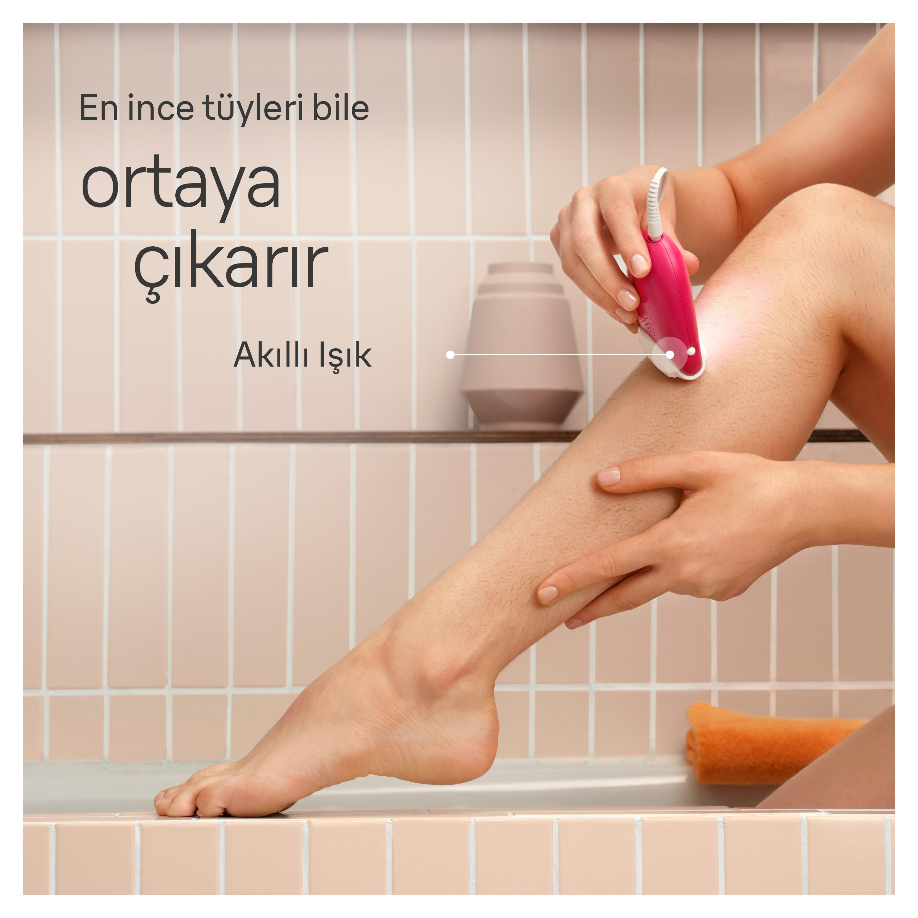 Bir kişi bacağında pembe bir epilatör kullanıyor. Sahne bir banyo. Arka plan duvarı gösteriyor.