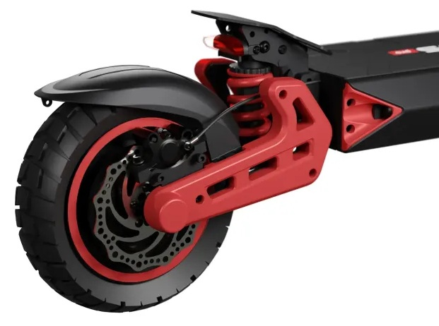 Zbliżenie tylnego koła hulajnogi elektrycznej. Czarna opona, czerwone akcenty na zawieszeniu i hamulcu. Hulajnoga jest czarno-czerwona.