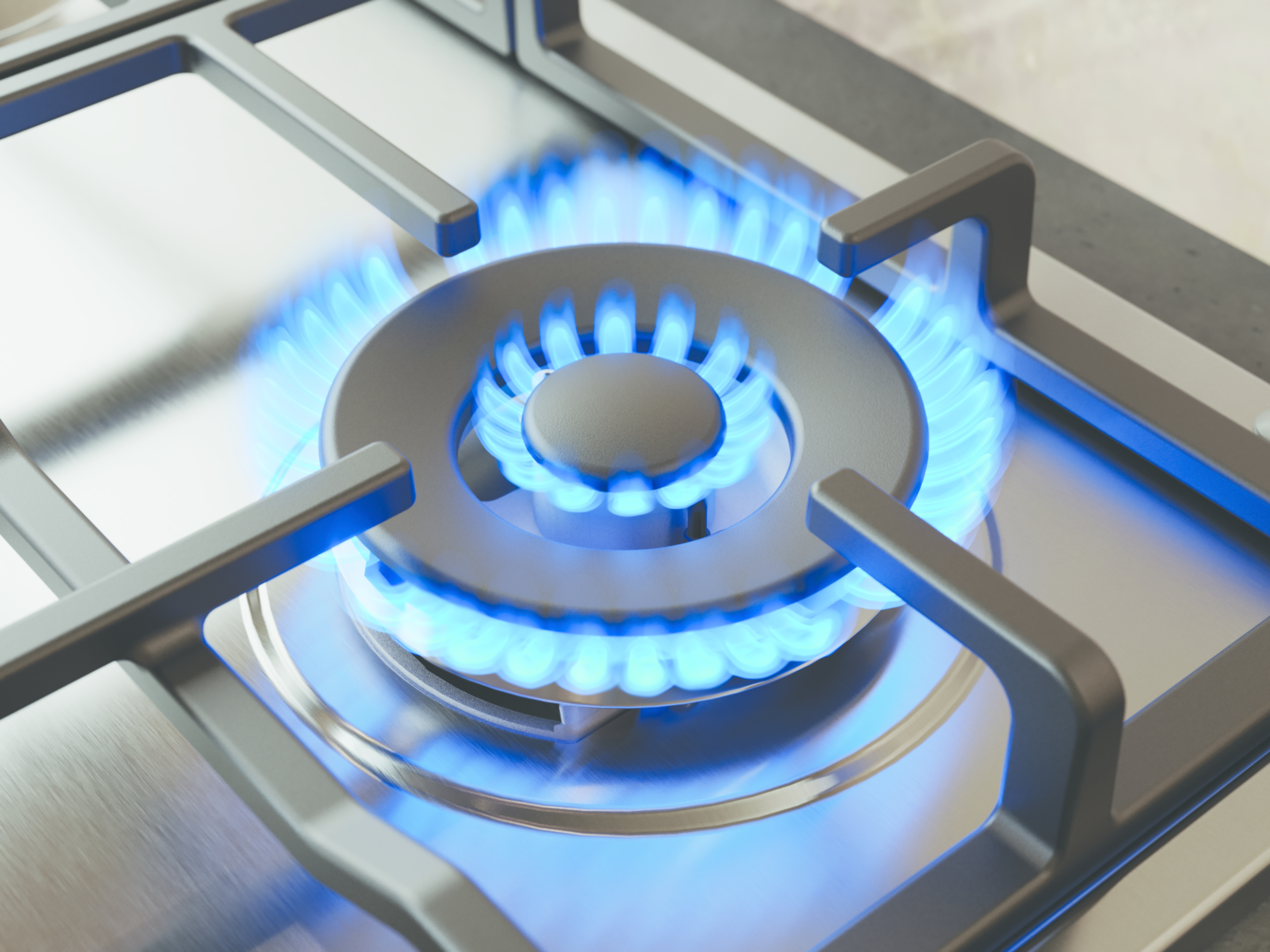 Zbliżenie palnika kuchenki gazowej z niebieskimi płomieniami. Palnik otoczony jest metalem i szarą powierzchnią.