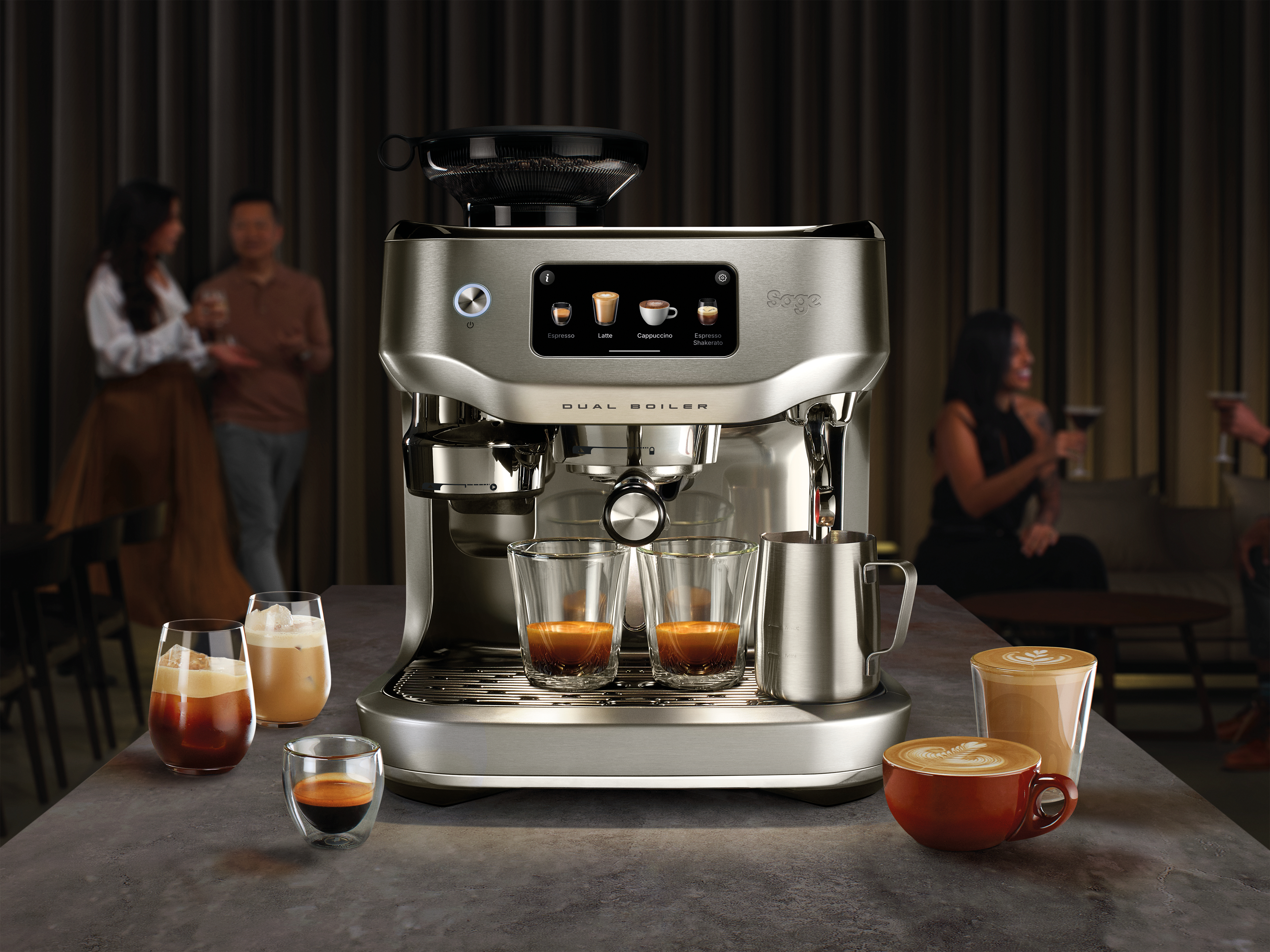 Espressomaschine mit Kaffeegetränken, zwei Personen im Hintergrund verschwommen und Kaffeetassen auf einem Tisch.