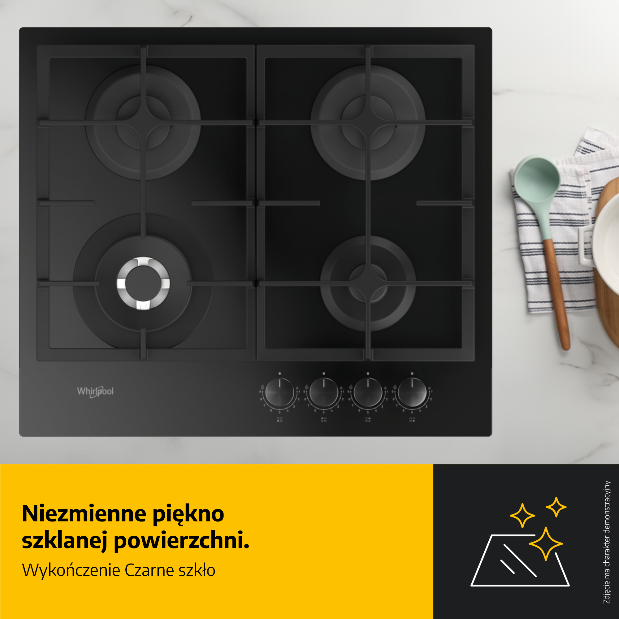 Czarna płyta grzejna ze szkła z czterema palnikami i pokrętłami. Na prawo chochla i miska na drewnianej desce.