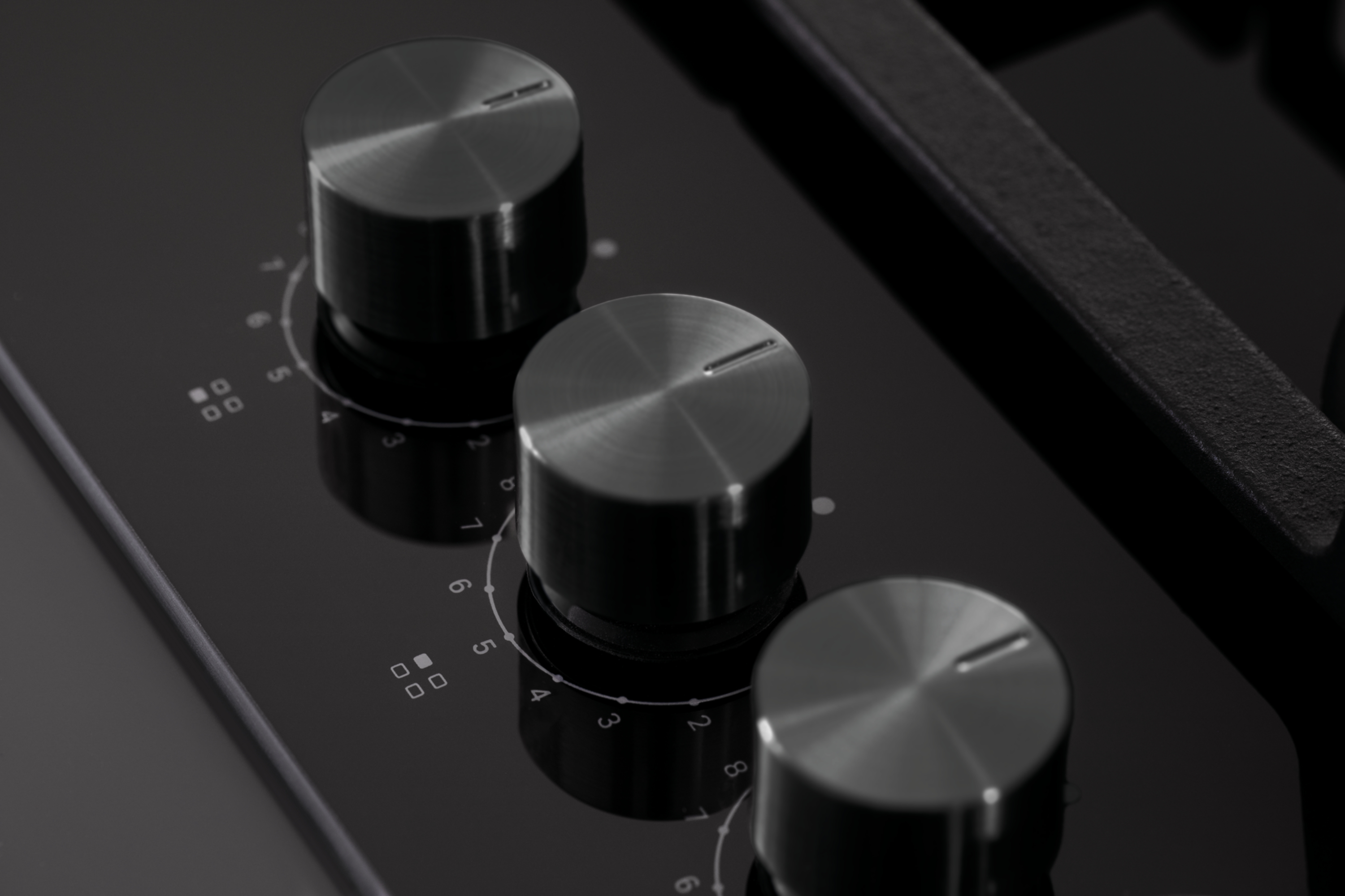 Zbliżenie płyty kuchennej z trzema metalowymi pokrętłami. Liczby i symbole widoczne na czarnej powierzchni.