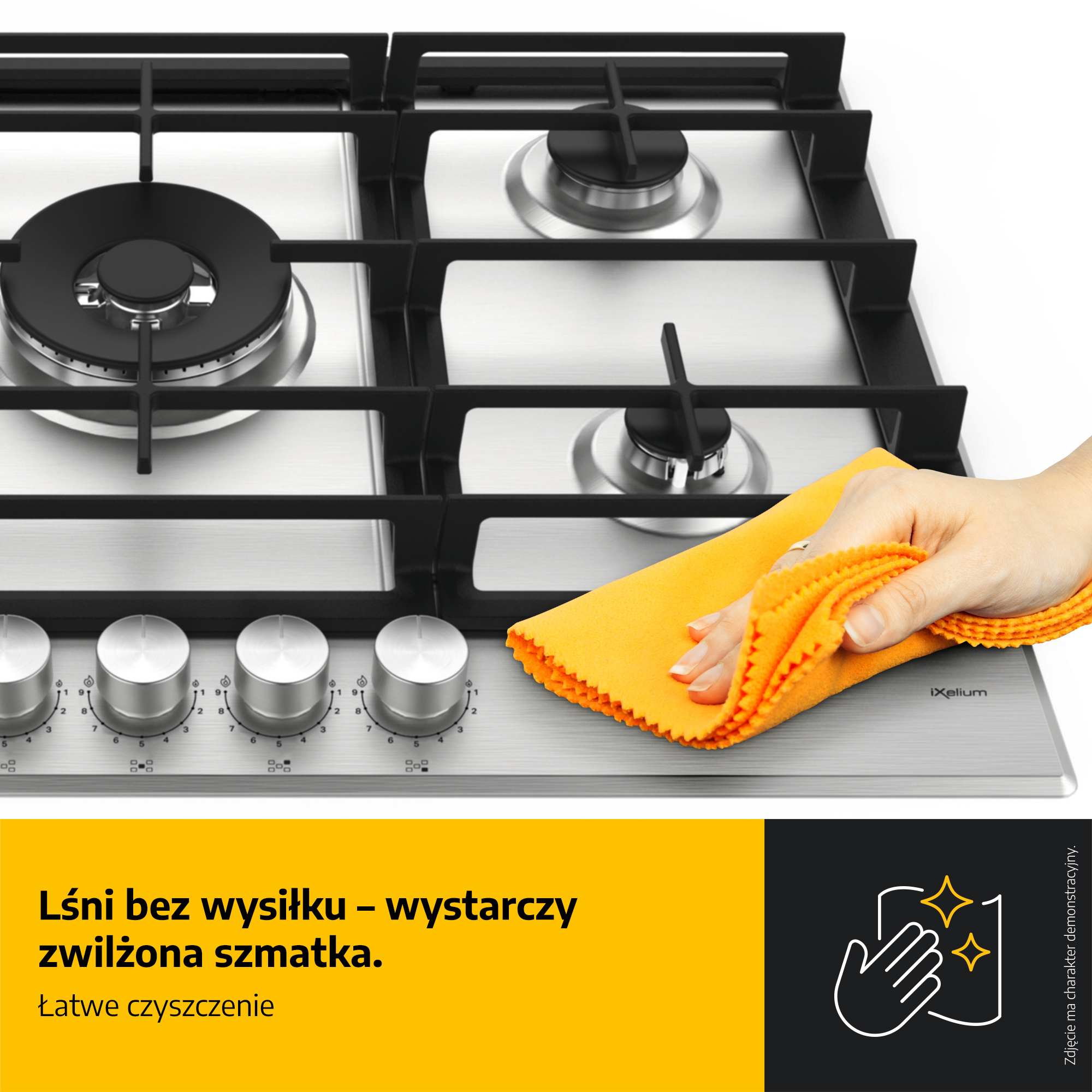 Ręka czyści stalową kuchenkę gazową pomarańczową szmatką. Widoczne są pokrętła i czarne ruszty.