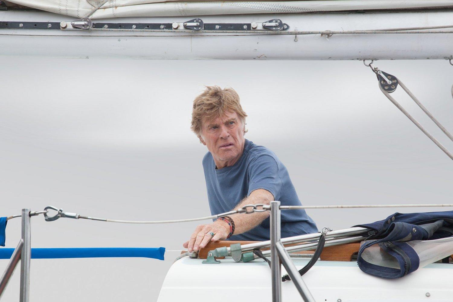 Ein älterer Mann auf einem Segelboot. Er trägt ein blaues Hemd und blickt nach links. Das Segel ist weiß, der Himmel grau.