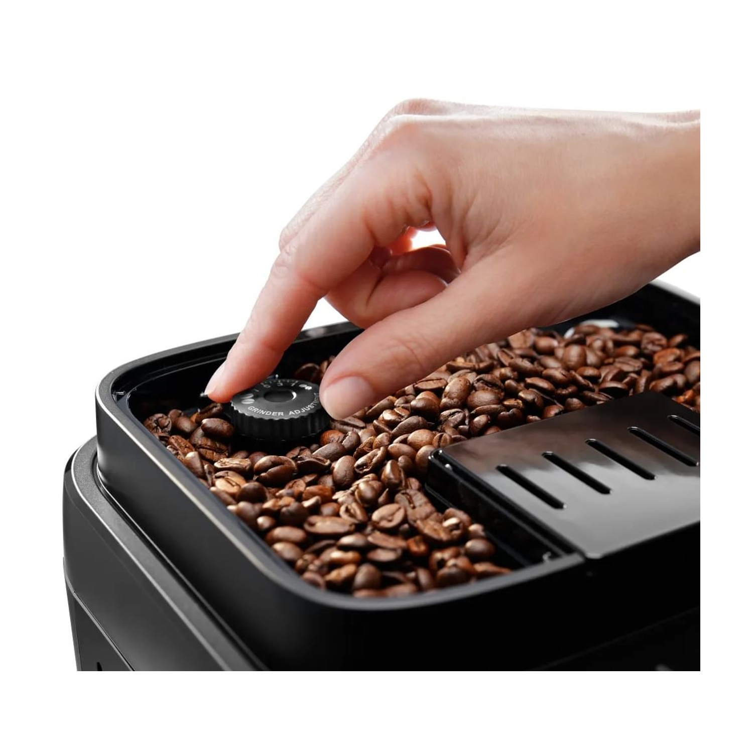 Una mano regola la manopola del macinacaffè su una macchina da caffè piena di chicchi di caffè marroni. Lo sfondo è bianco.