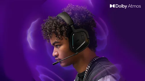 Egy személy fekete fejhallgatóval és mikrofonnal, ezüst lánccal, lila háttérrel, Dolby Atmos logóval.