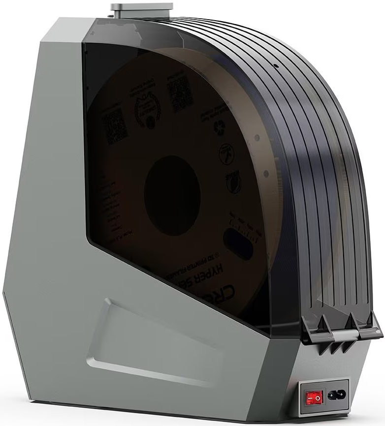 Un sécheur de filament gris avec un couvercle transparent noir. À l'intérieur, une bobine de filament marron est visible. Un interrupteur d'alimentation rouge est à droite.