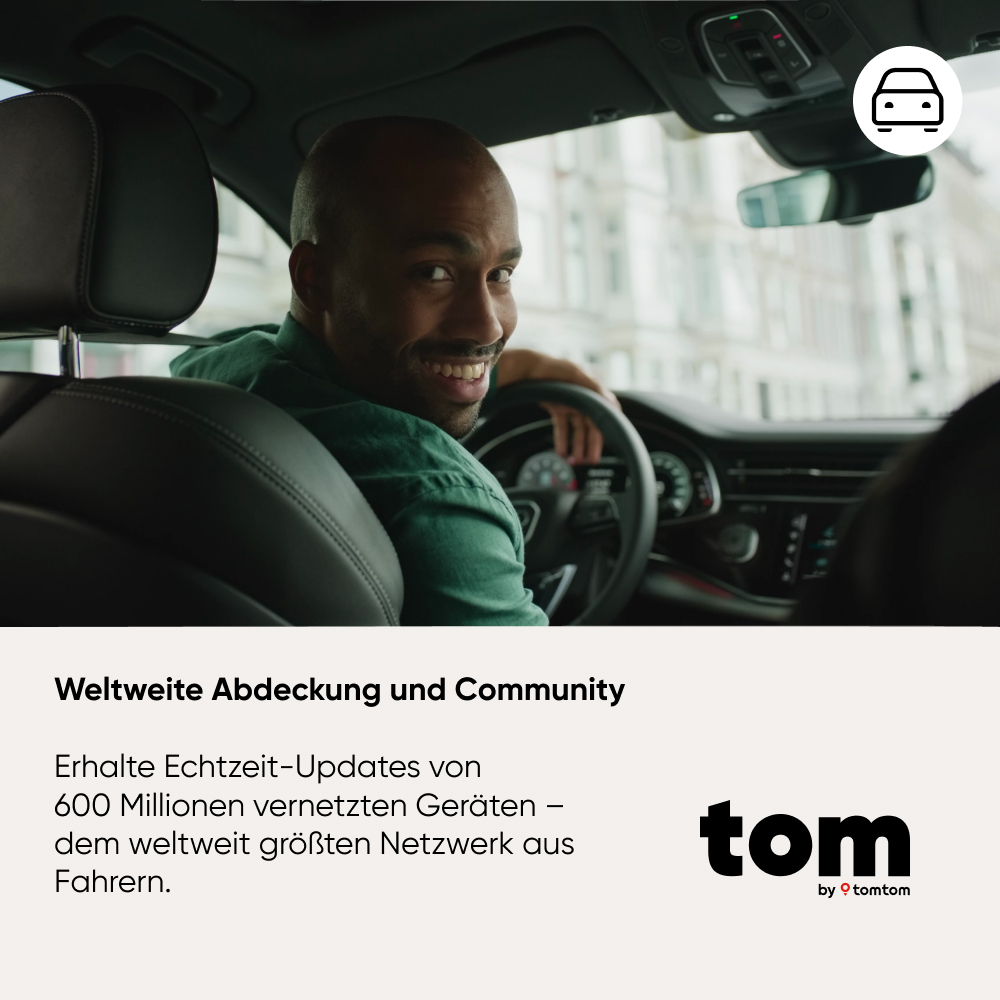 Ein lächelnder schwarzer Mann im Auto blickt zurück zum Betrachter. Er hält das Lenkrad. Das TomTom-Logo ist sichtbar.