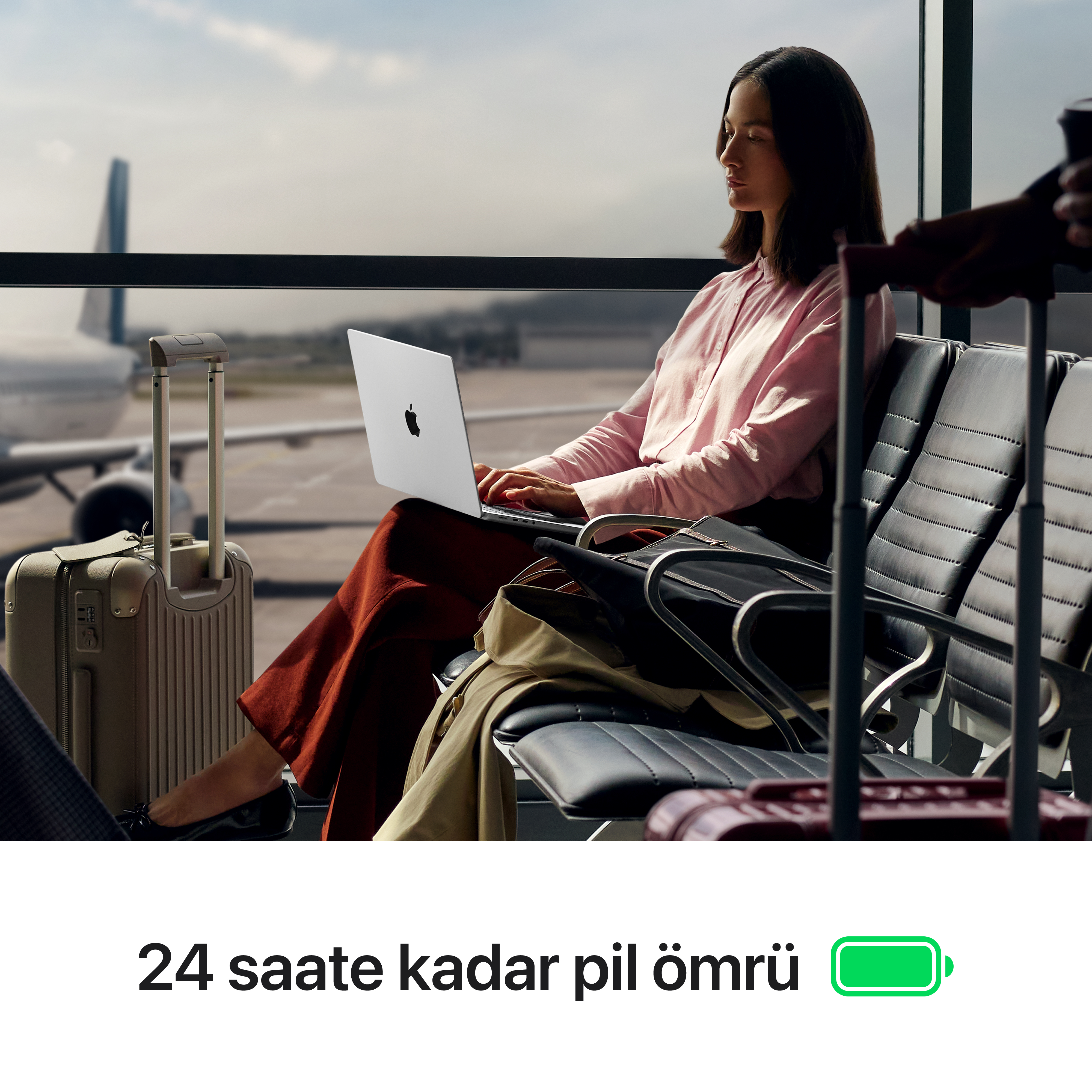 Havaalanında dizüstü bilgisayar kullanan bir kadın. Bagaj ve uçak görünür. Görüntüde bir pil simgesi var.