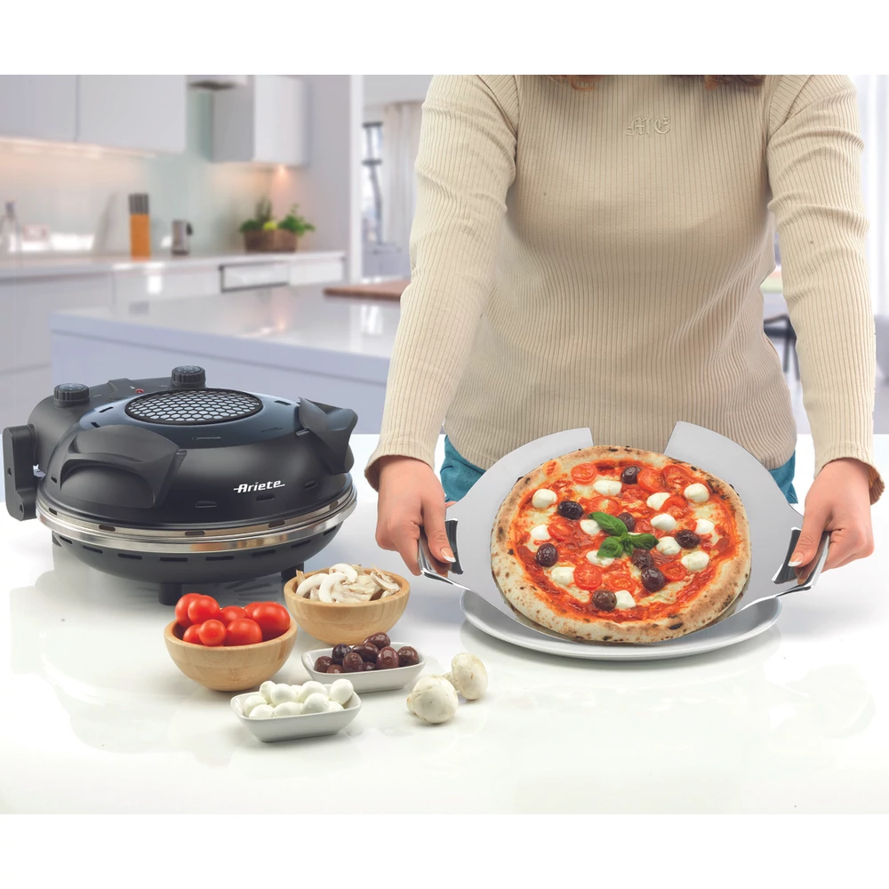 Egy személy pizzát tart egy lapáton. Egy pizzakemence és olyan hozzávalók, mint a paradicsom, gomba és mozzarella közelben.