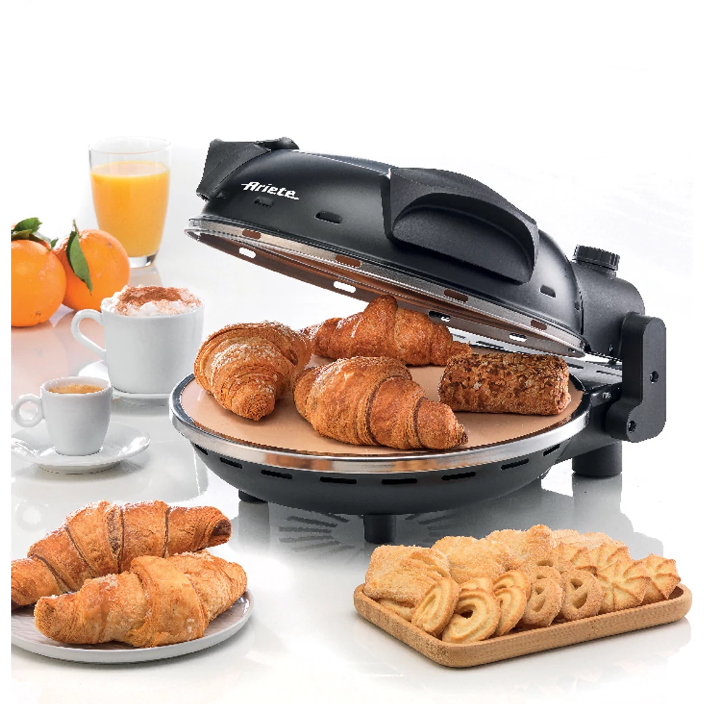 Fekete Ariete croissantkészítő croissantokkal, kávéval, narancsokkal és sütikkel fehér felületen.