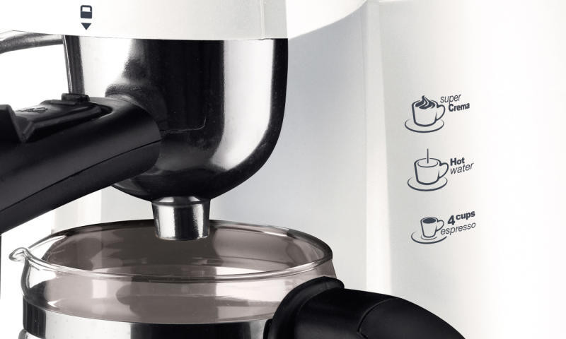 Közelkép egy fehér és fekete kávéfőzőről. Egy üvegkancsó ül az adagoló alatt. A címkék a super crema, a forró víz és az eszpresszó feliratokat jelzik.