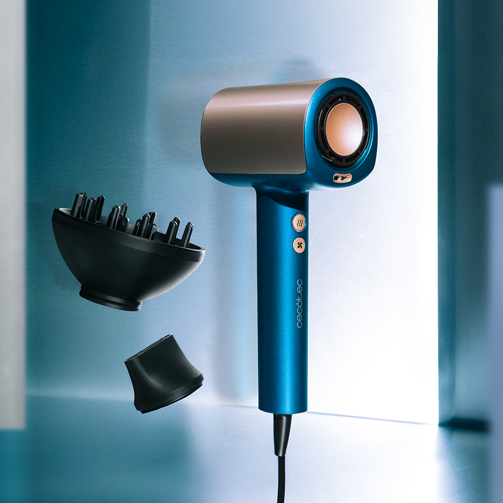 Un secador de pelo azul y dorado con accesorios, flotando sobre un fondo azul, iluminado desde la derecha.