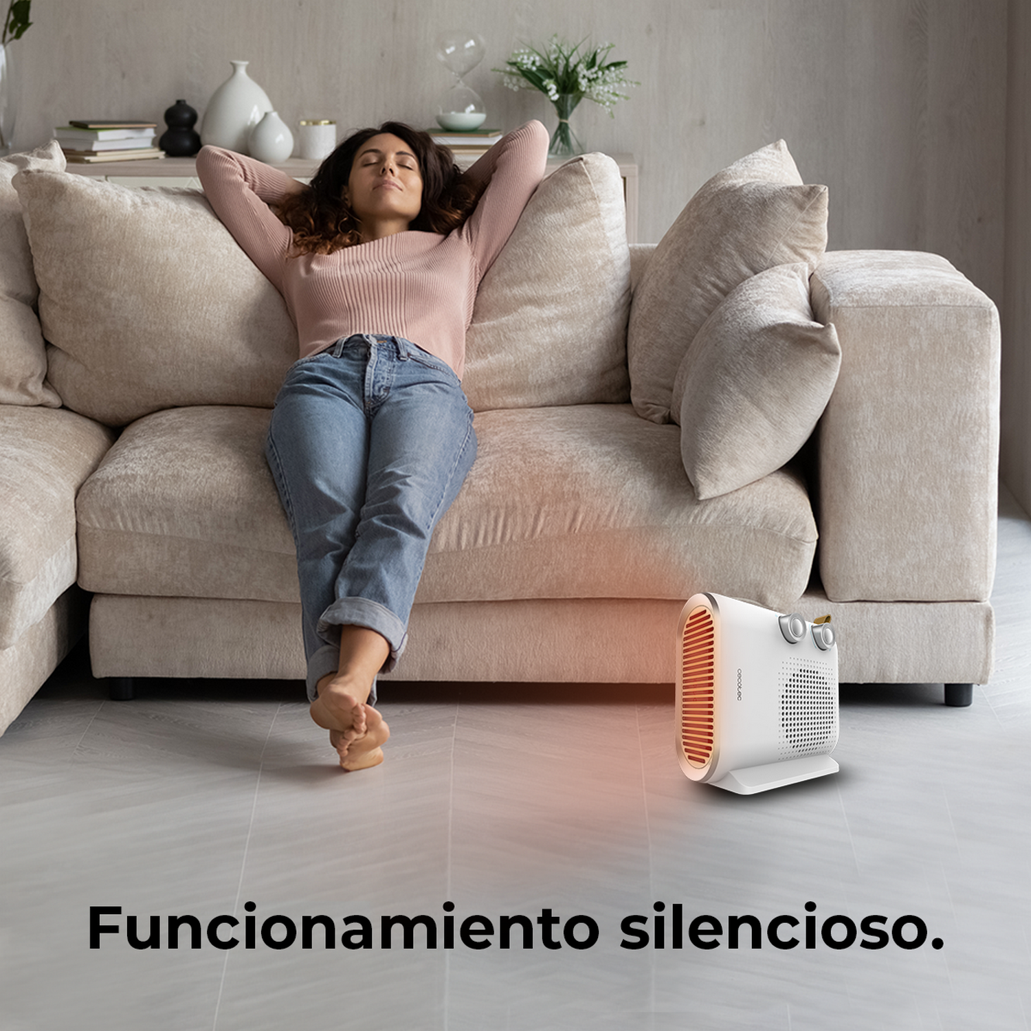Mujer relajándose en un sofá beige, con los brazos detrás de la cabeza, ojos cerrados. Calentador blanco en primer plano. Texto: funcionamiento silencioso.